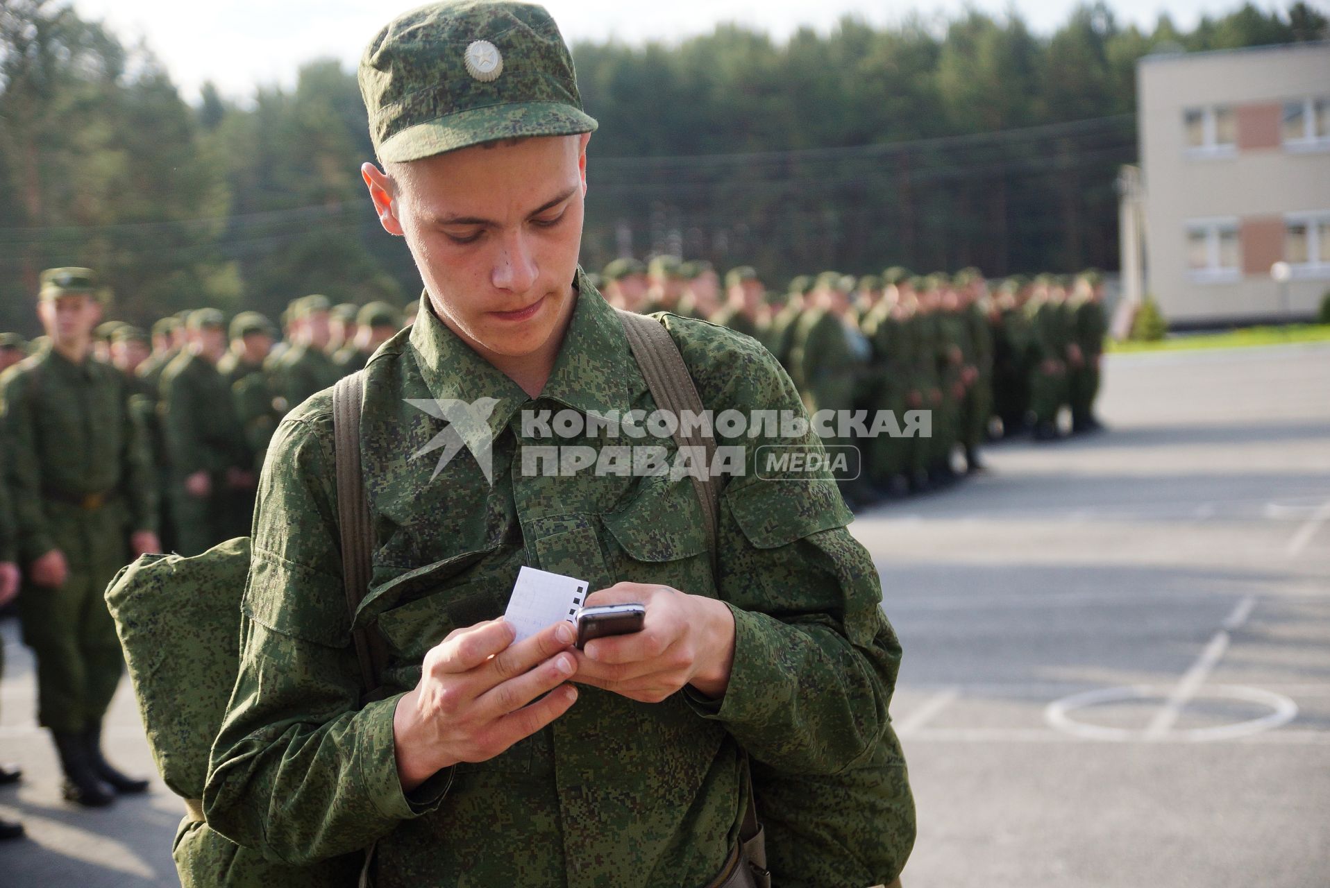 Призывник звонит по мобильному телефону перед строем солдат.