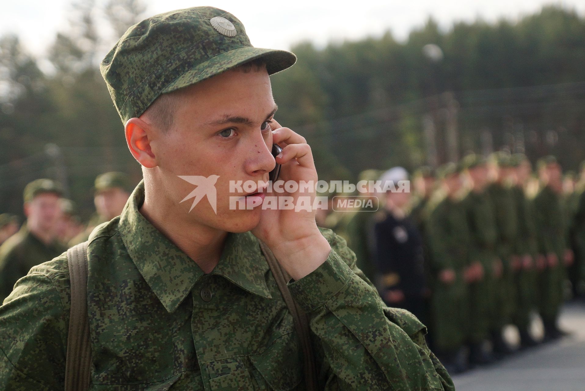 Призывник звонит по мобильному телефону перед строем солдат.