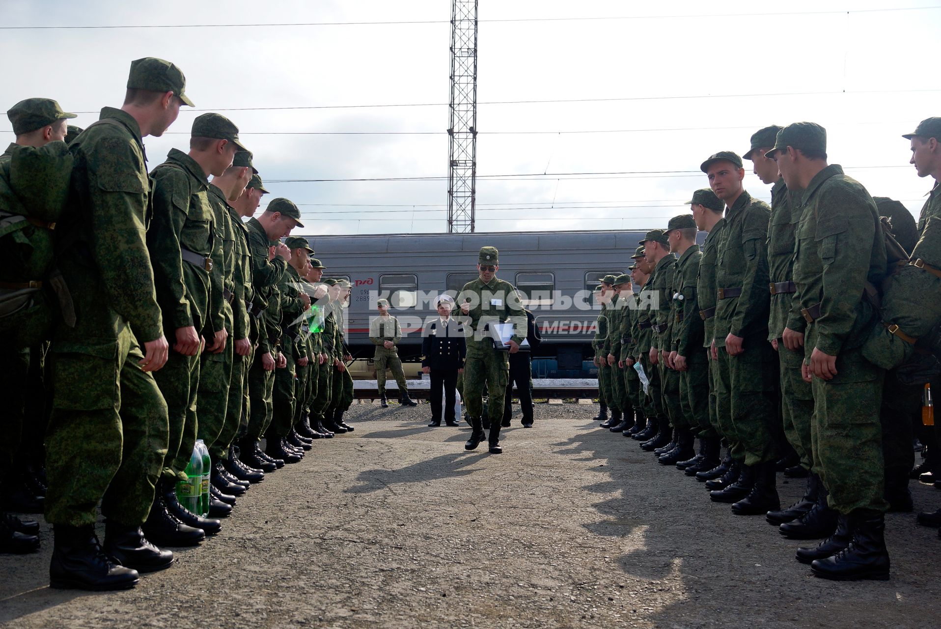 Офицер проходит вдоль строя солдат стоящих перед поездом на вокзале.
