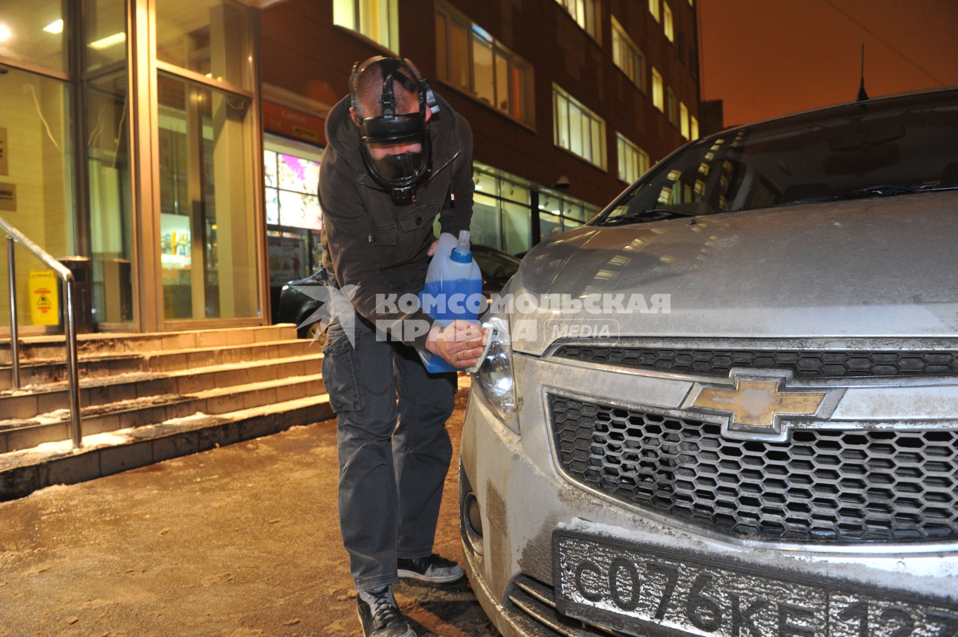 Молодой человек протирает фары автомобиля незамерзающей жидкостью.