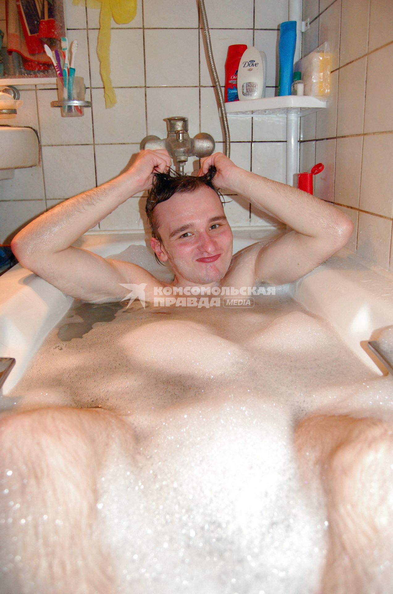 Парень, лежащий в ванне с пеной, моет голову.