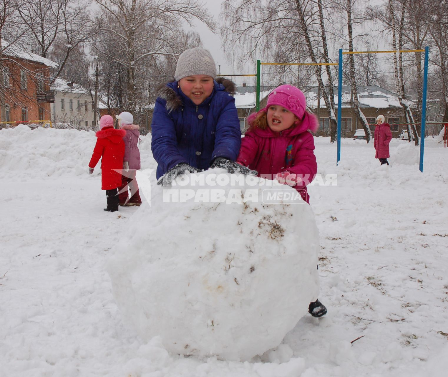 Дети лепят большой ком снега для снеговика.