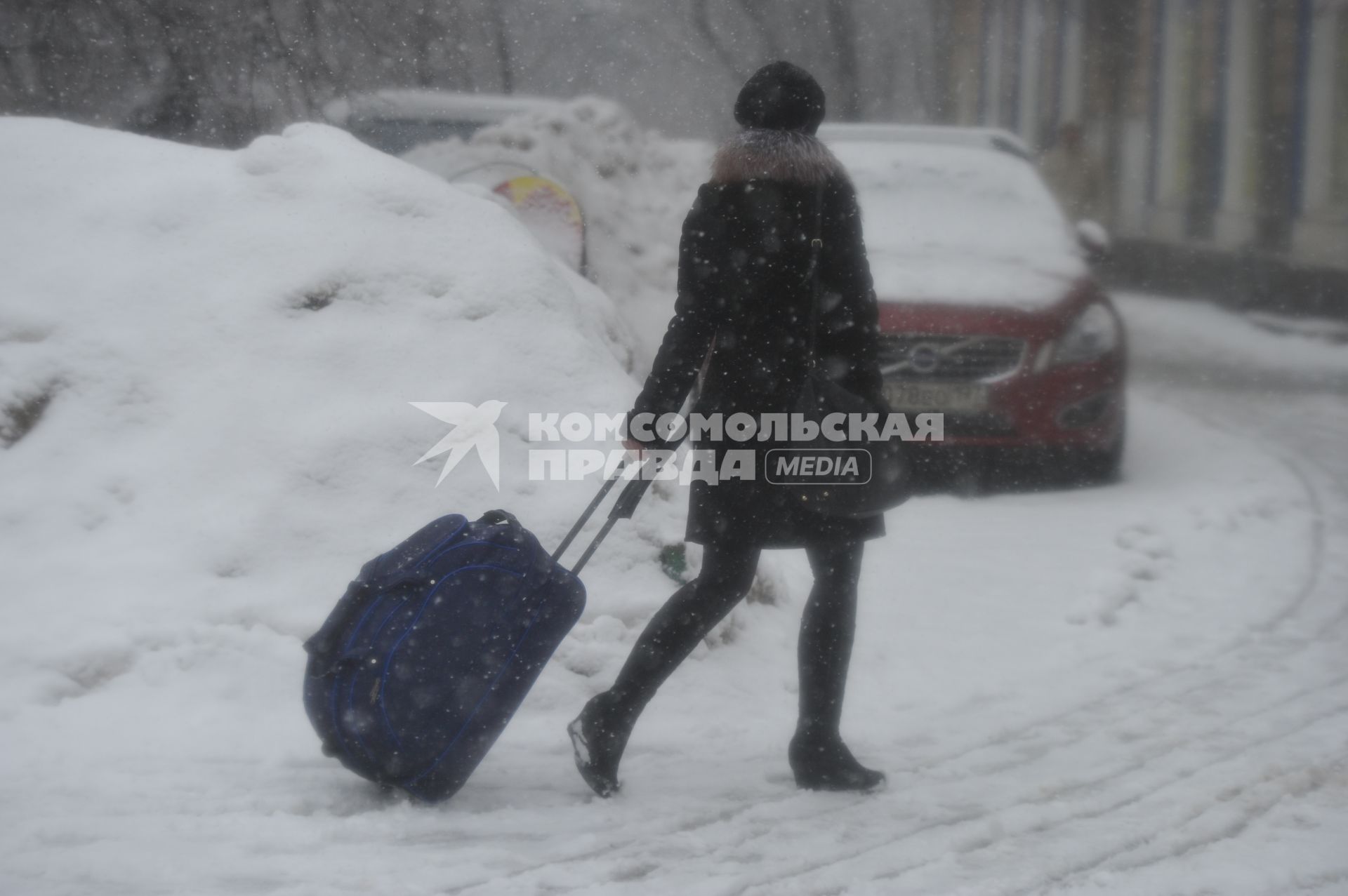 Снегопад. На снимке:  девушка с чемоданом на колесиках