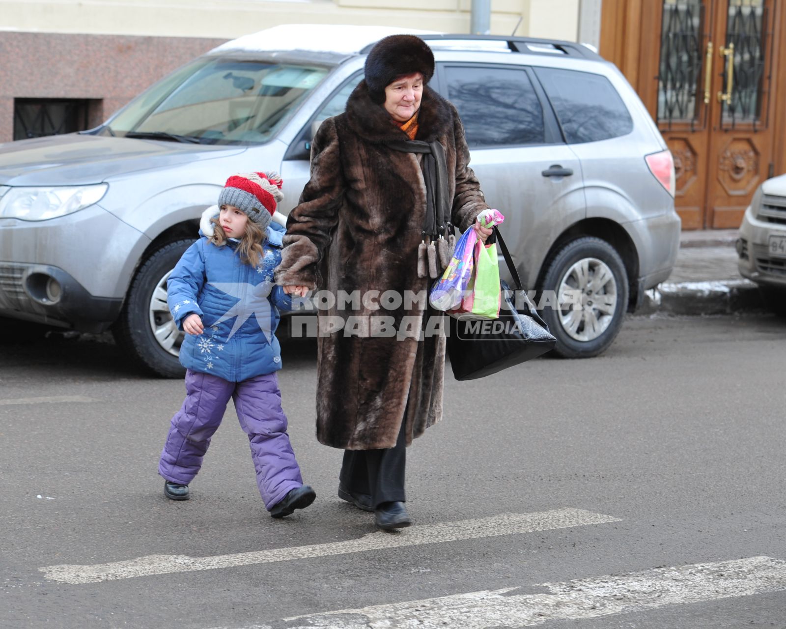 Пожилая женщина с ребенком переходят дорогу.