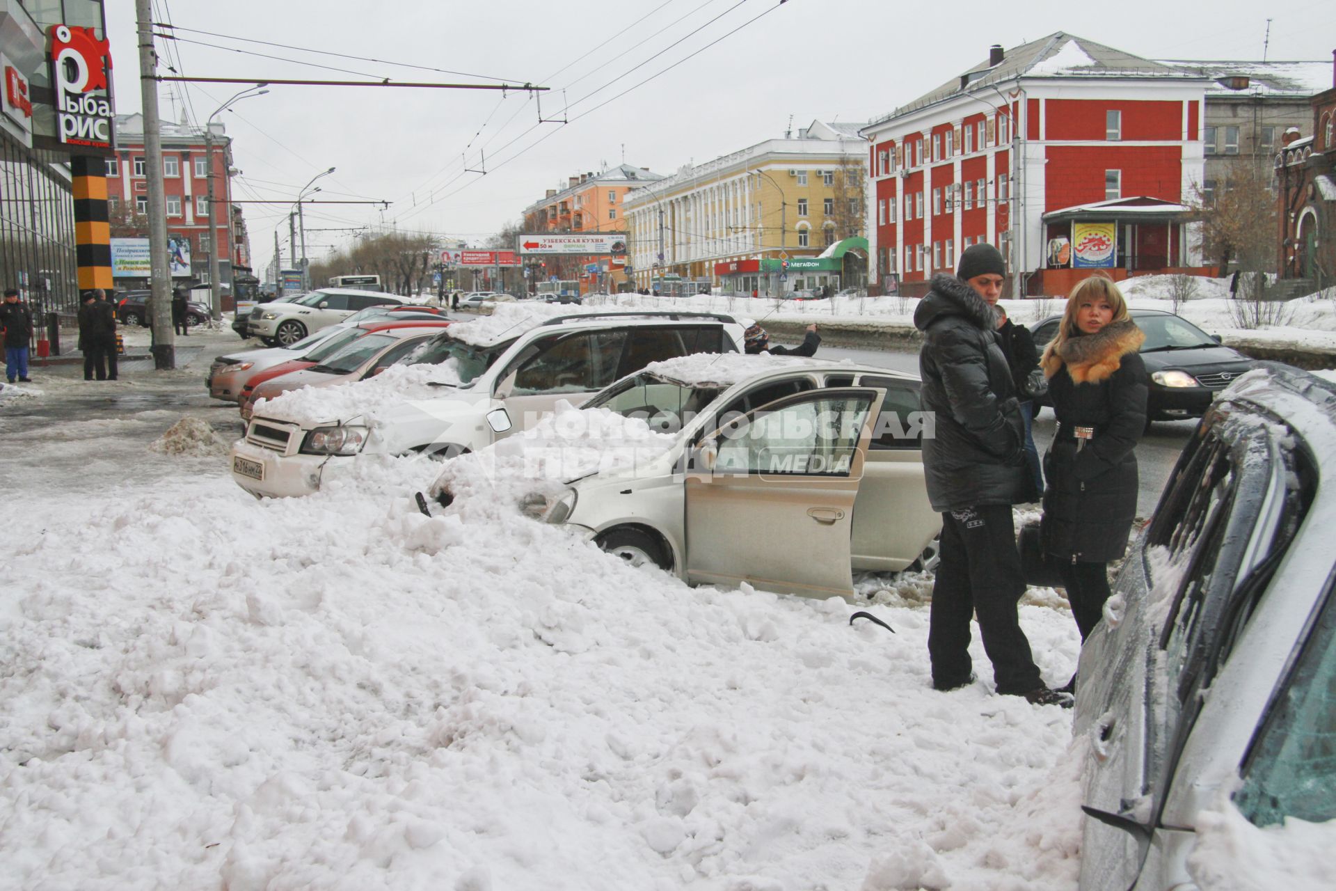 Снежная лавина обрушилась с крыши дома на тротуар и припаркованные автомобили в Барнауле. На снимке: люди стоят у поврежденных автомобилей засыпанных снегом.