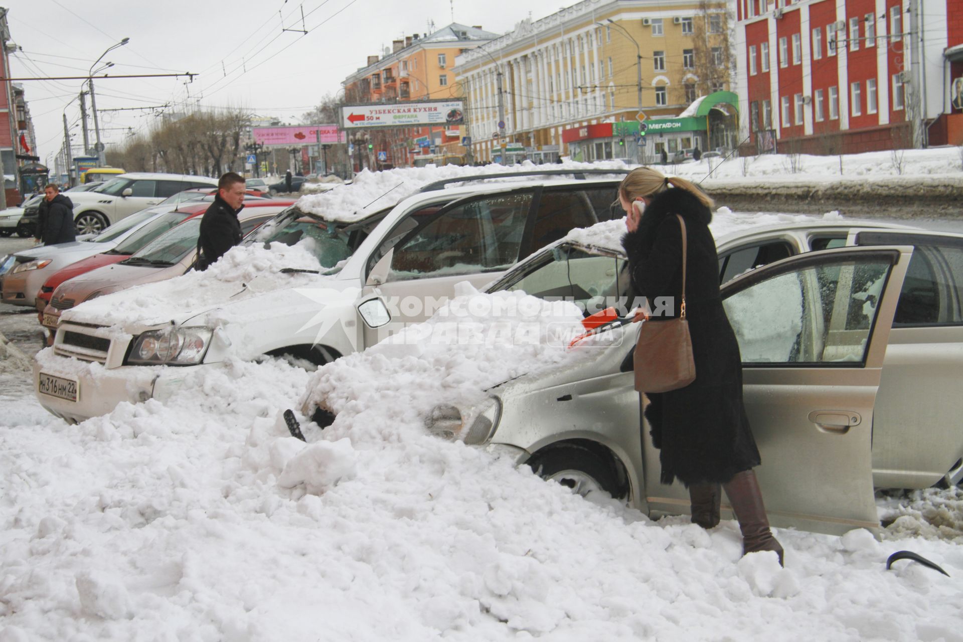 Снежная лавина обрушилась с крыши дома на тротуар и припаркованные автомобили в Барнауле. На снимке: люди стоят у поврежденных автомобилей засыпанных снегом.