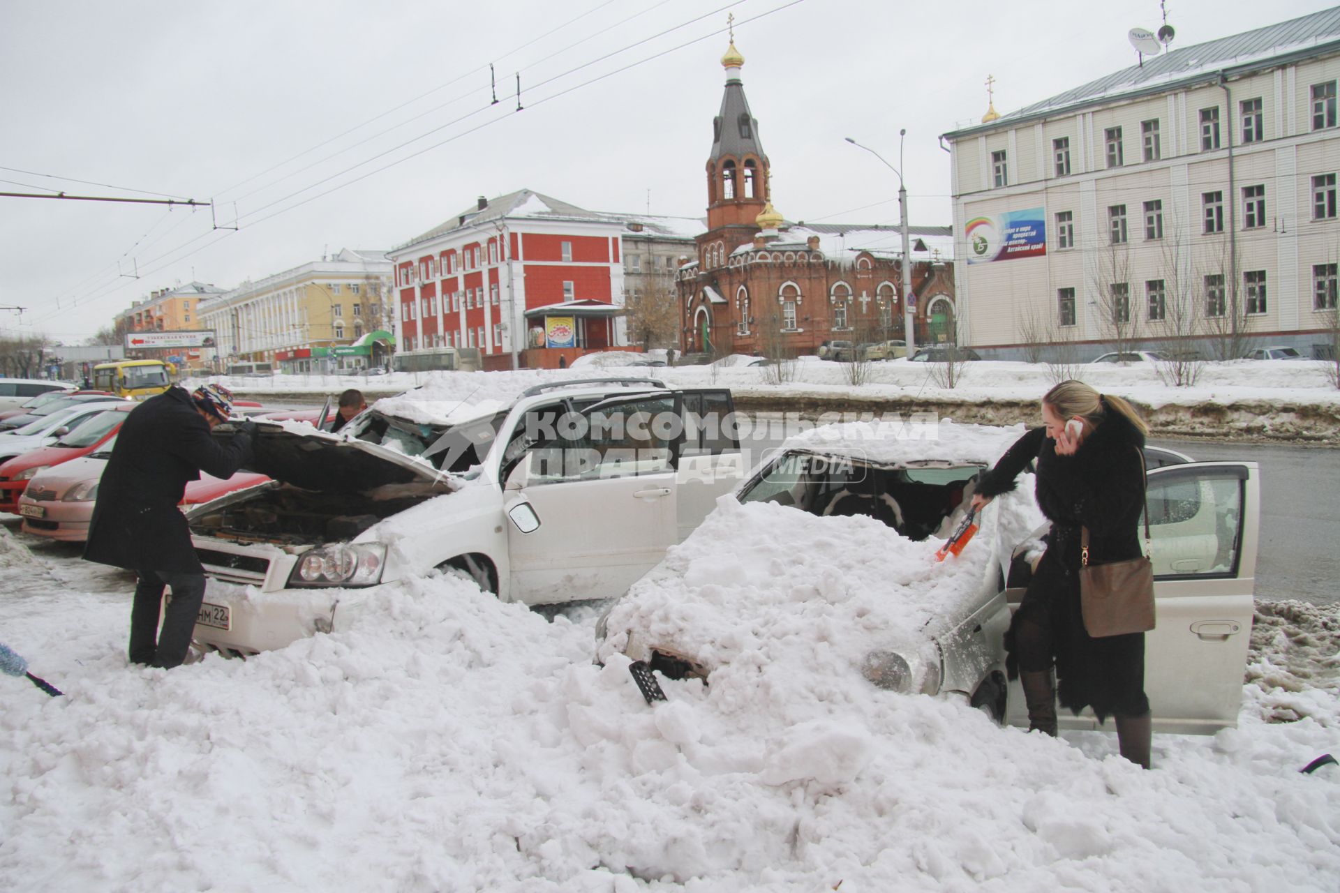 Снежная лавина обрушилась с крыши дома на тротуар и припаркованные автомобили в Барнауле. На снимке: люди стоят у поврежденных автомобилей засыпанных снегом.