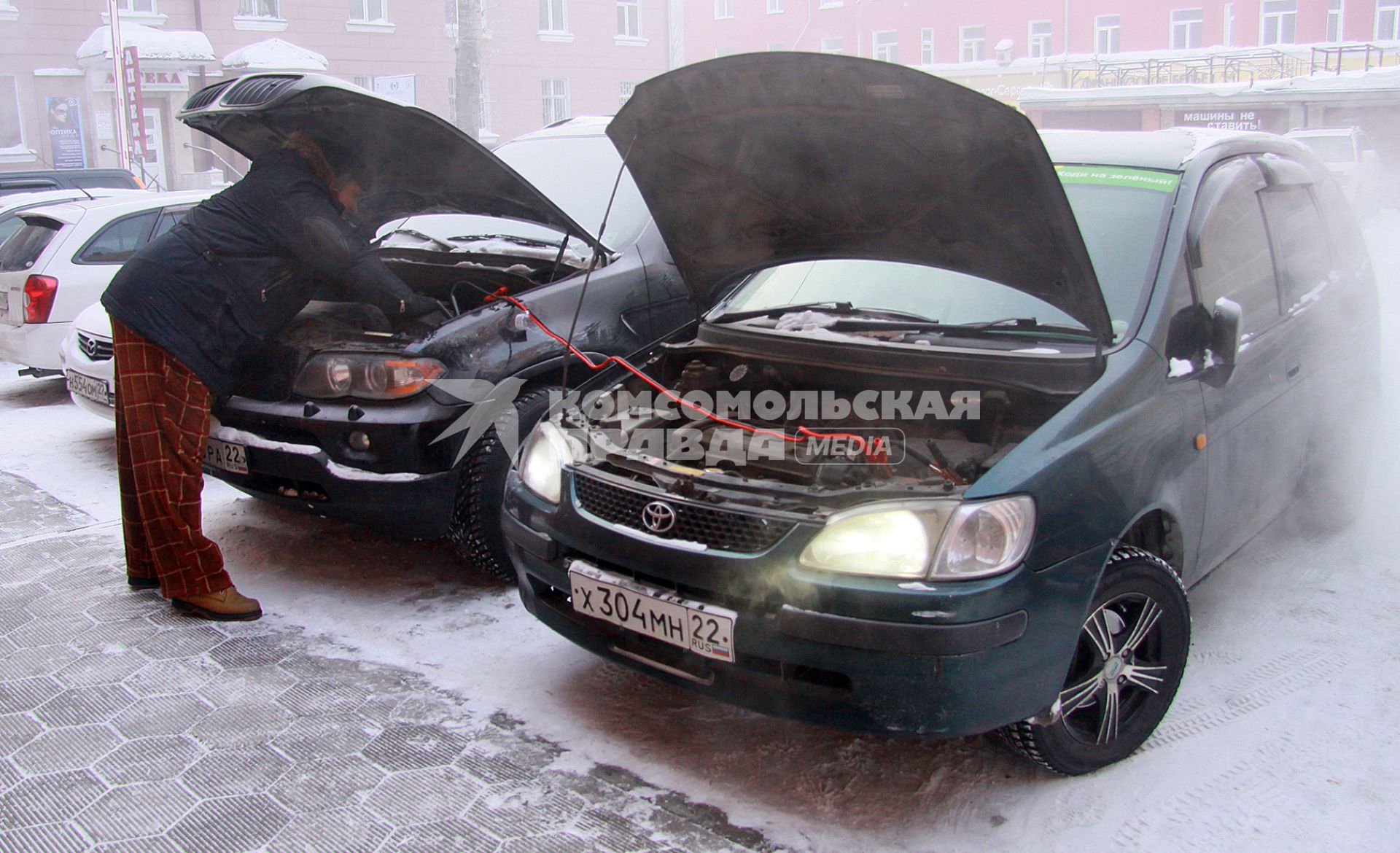 Водитель заводит автомобиль с помощью проводов `прикуривая` от другого автомобиля.