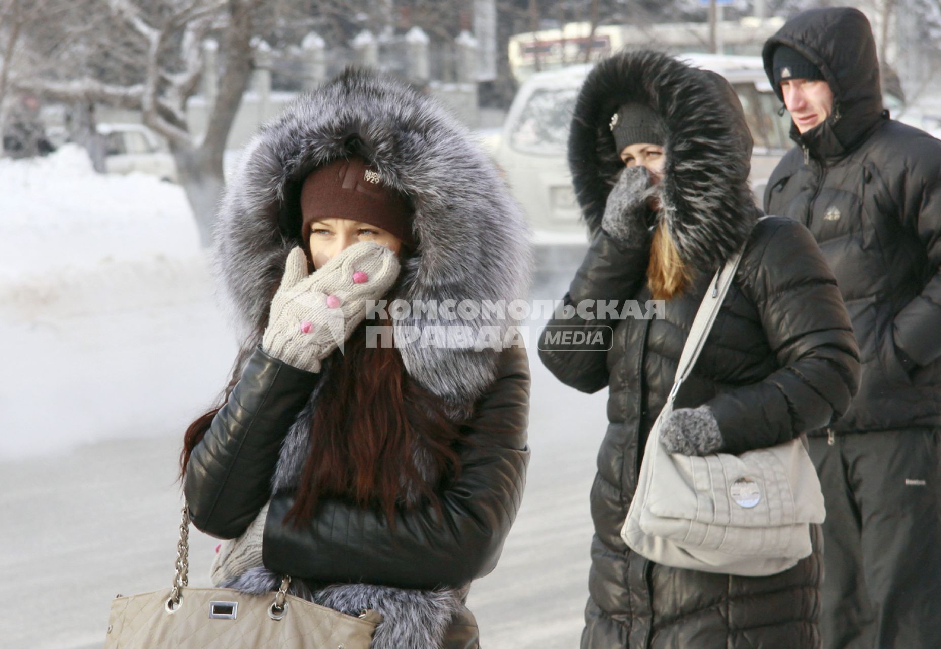Люди на остановке общественного транспорта закрывают лицо руками от мороза.