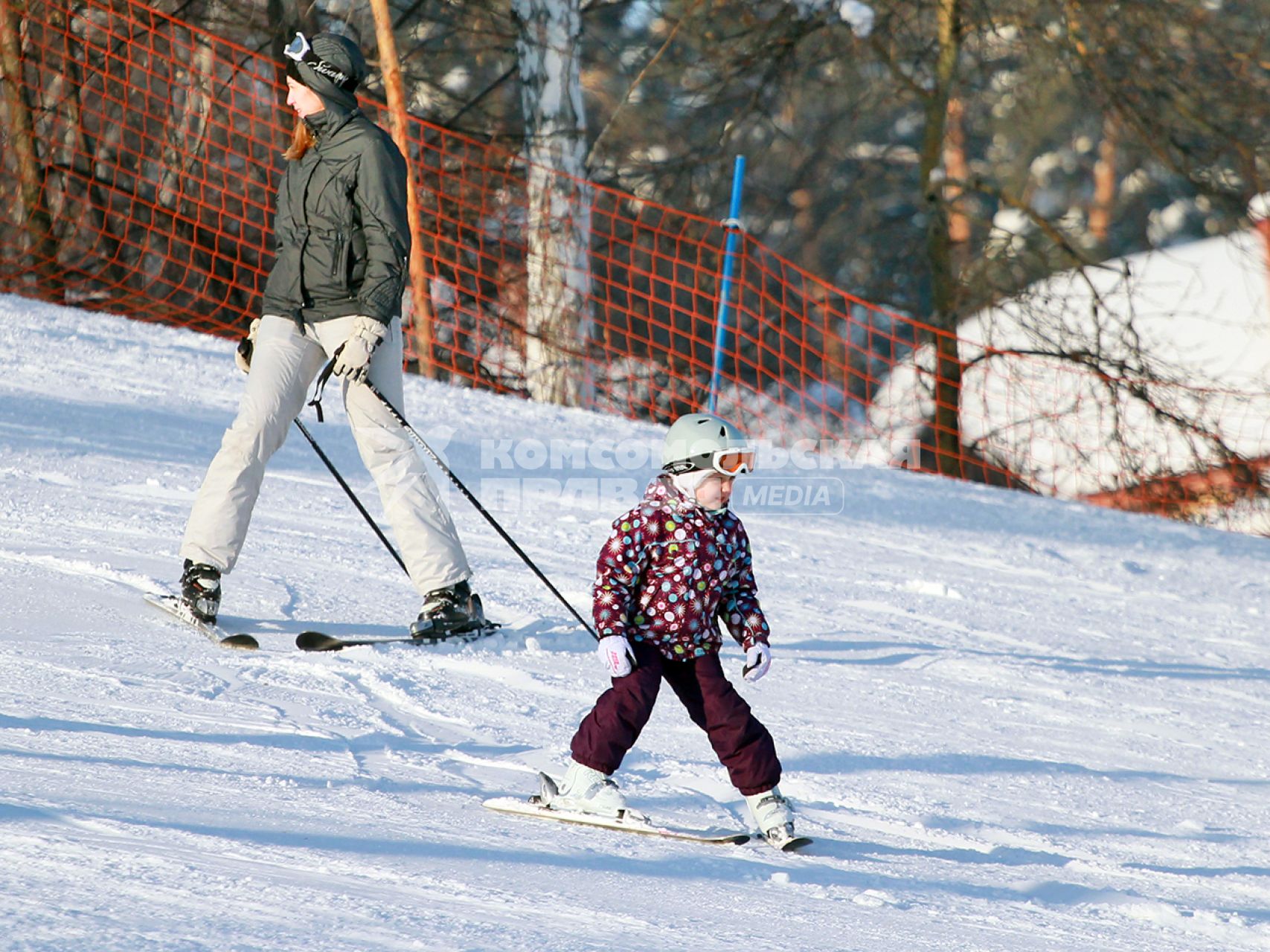 Маленькая девочка спускается с горы на горных лыжах, сзади спускается инструктор.
