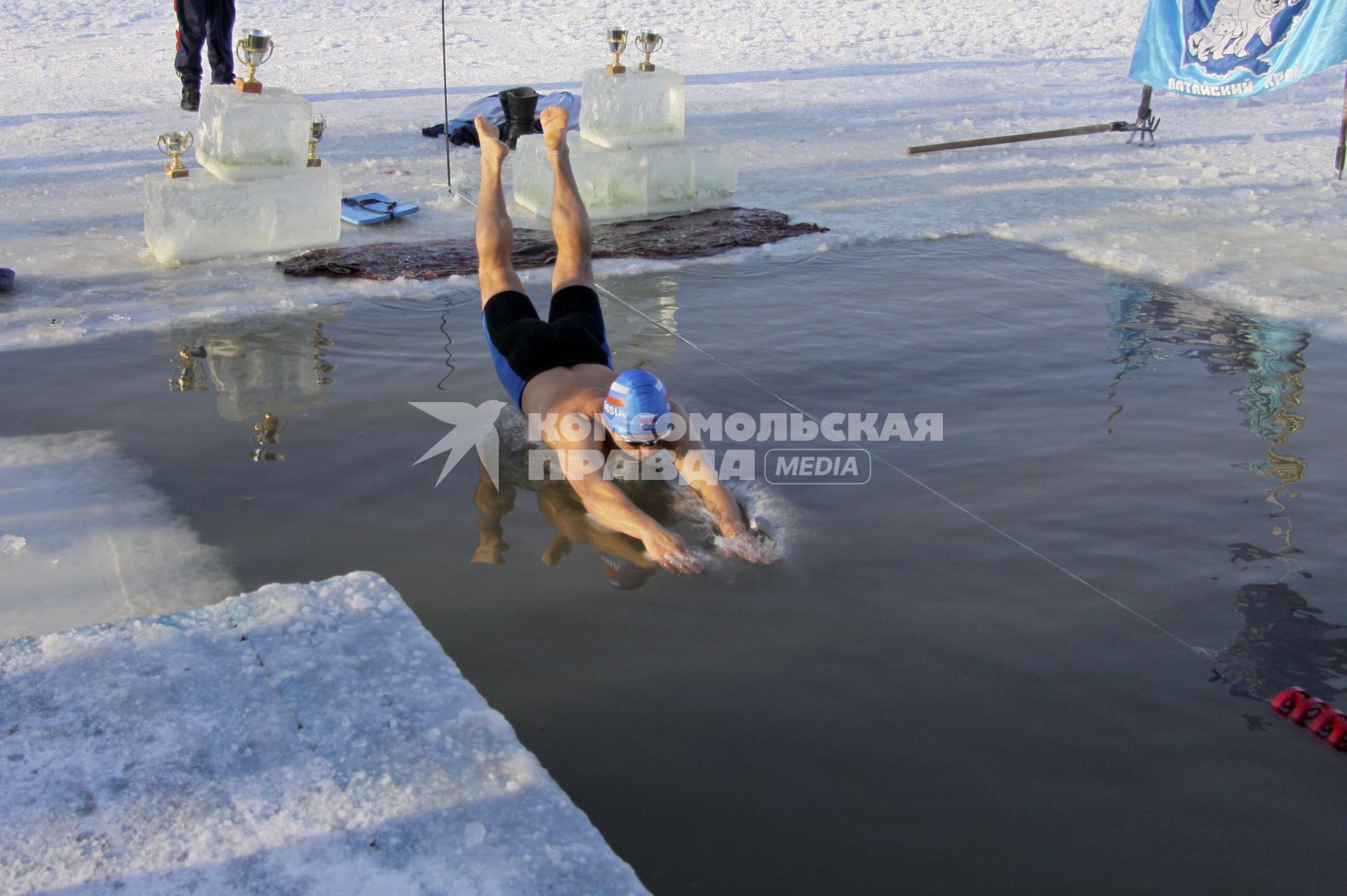 На соревновании по моржеванию зимой мужчина пловец прыгает в ледяную воду проруби.