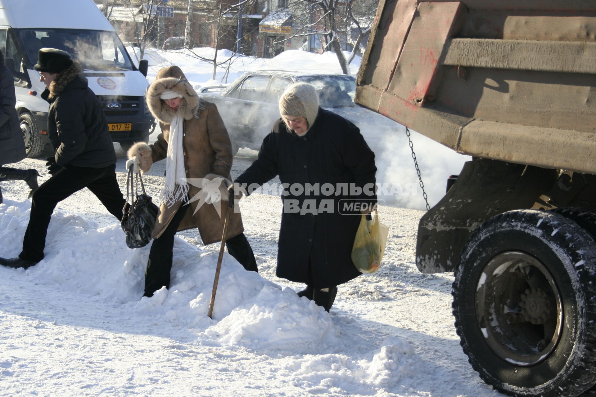 Пешеходы переходя улицу преодолевают большие снежные сугробы.