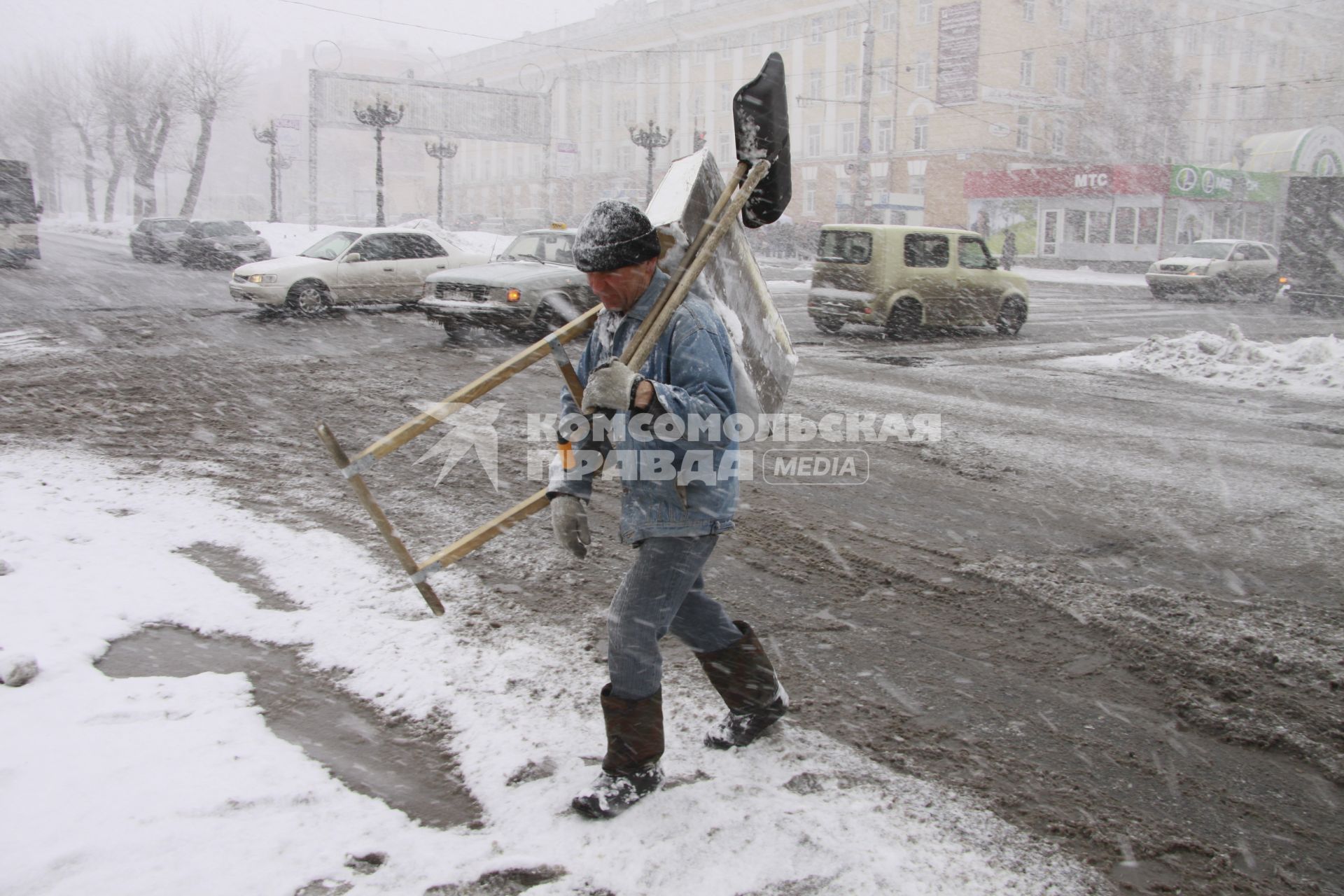 Дворник с лопатами переходит улицу во время сильного снегопада.