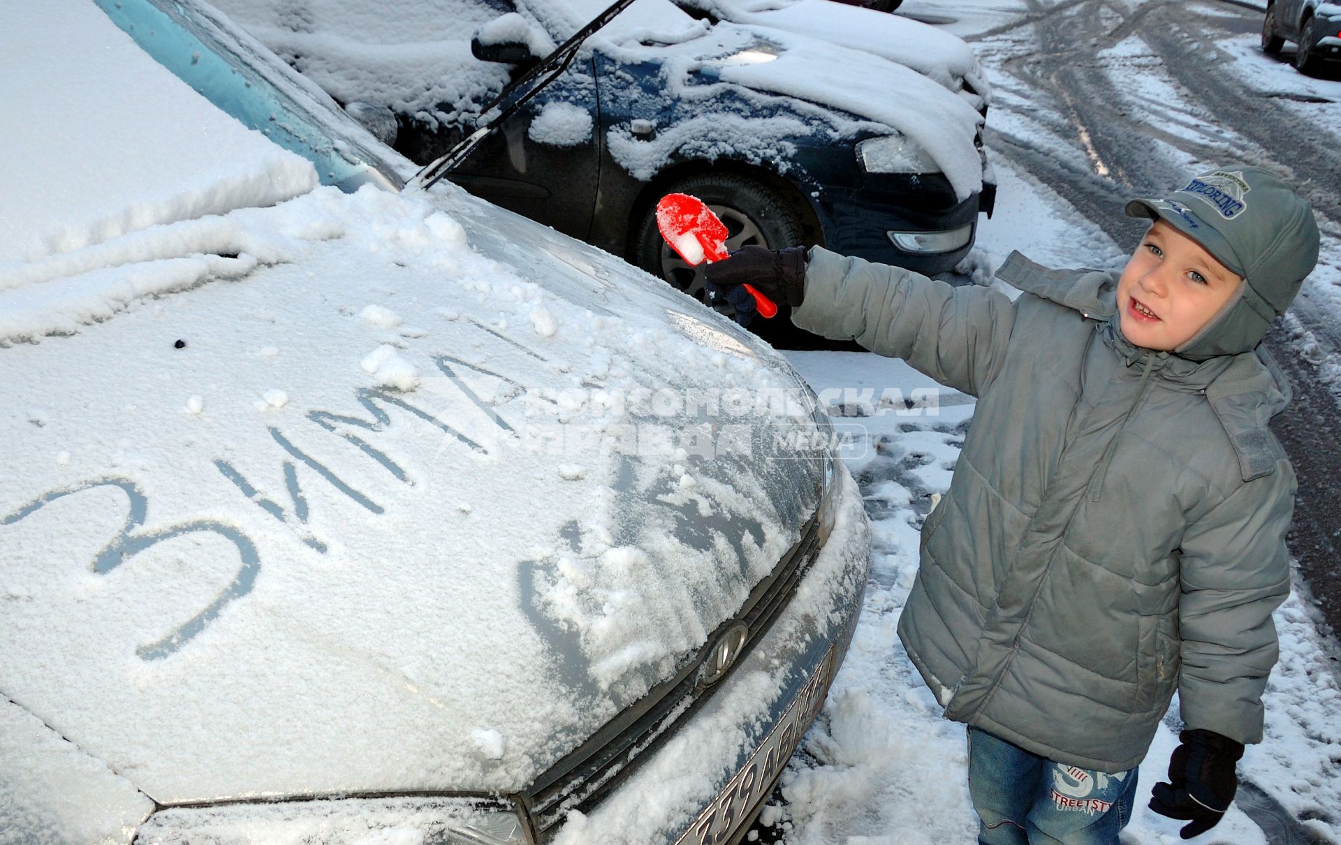 Ребенок рядом с автомобилем, на капоте которого написано: `Зима`.