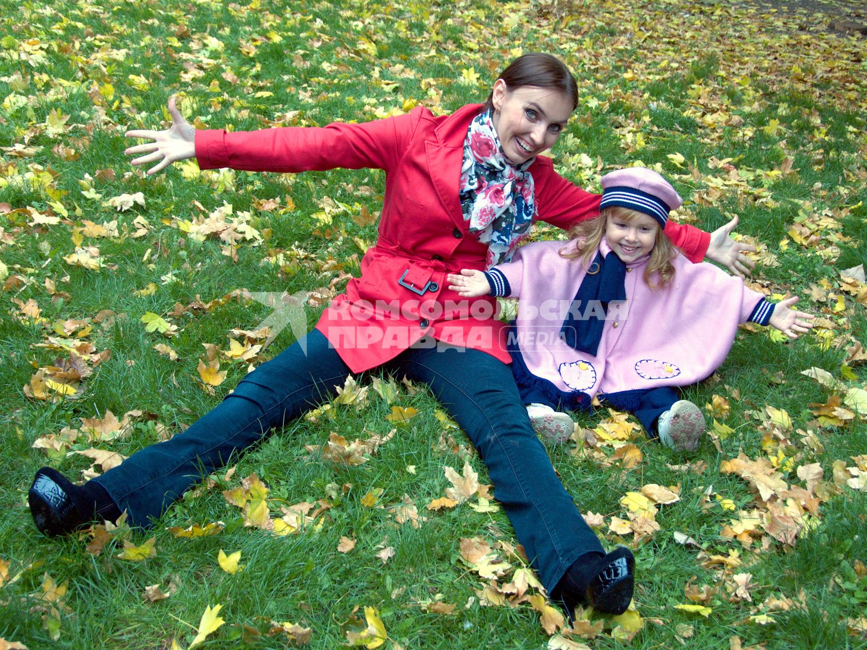 Девушка с ребенком на зеленой лужайке с опавшей осенней листвой.