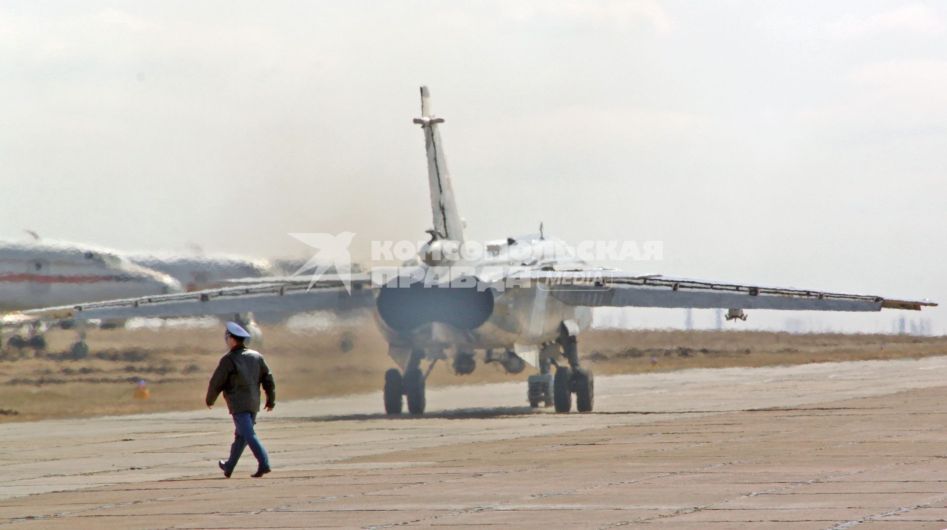 Военный идет по летному полю на фоне работающих двигателя военного самолета фронтового бомбардировщика СУ-24М.