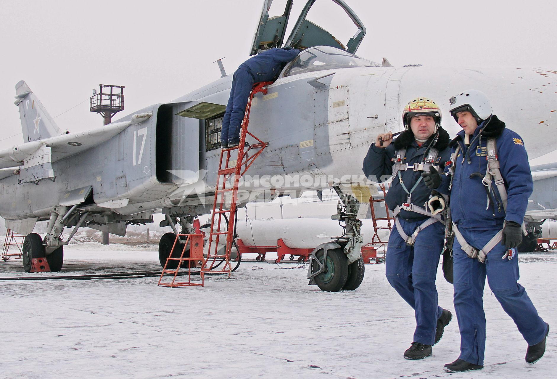 Два пилота идут разговаривают на фоне техника и военного самолета фронтового бомбардировщика СУ-24М.
