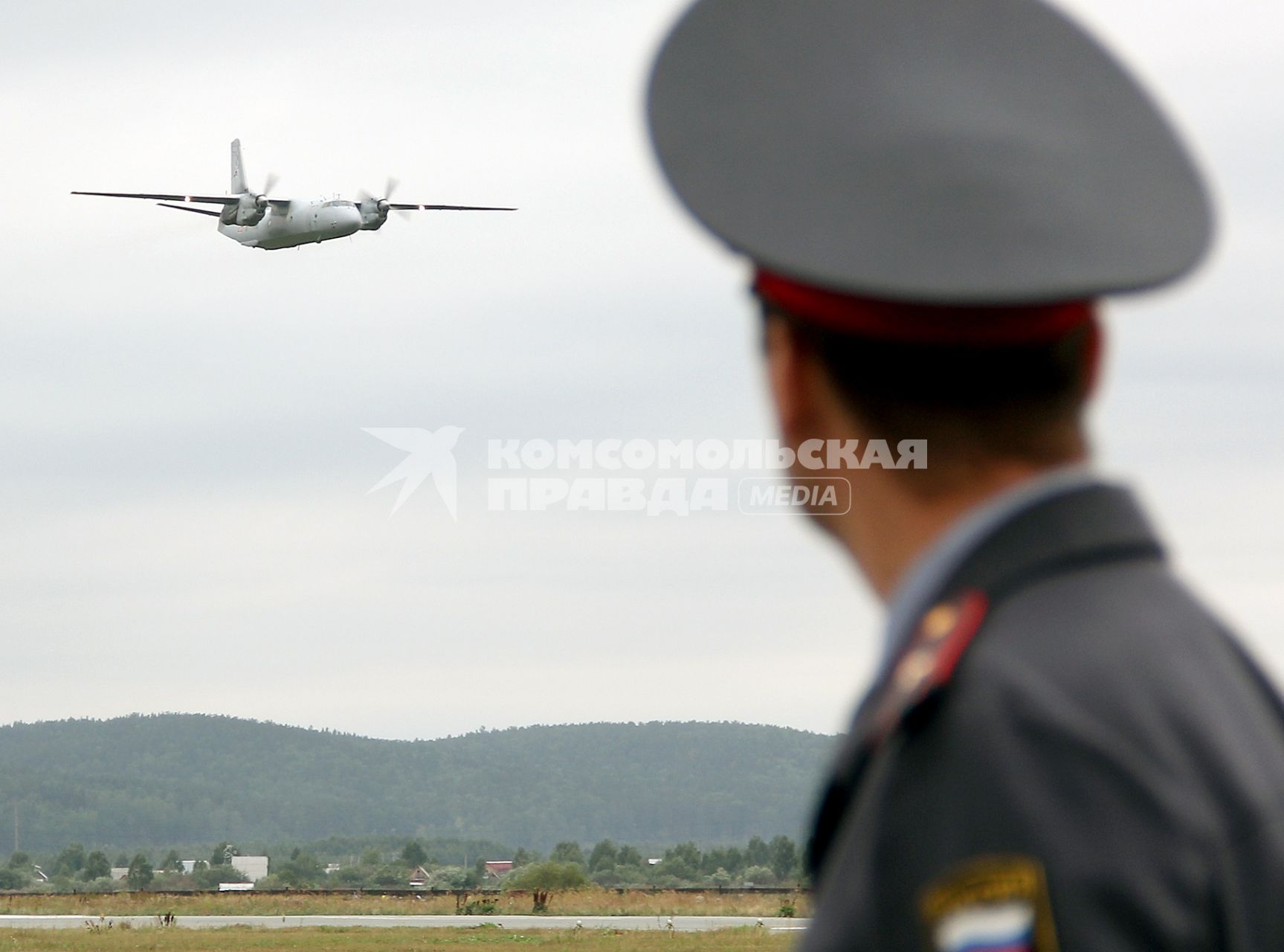 Полицейский смотрит на военно-транспортный самолет АН-26КПА ВВС России.