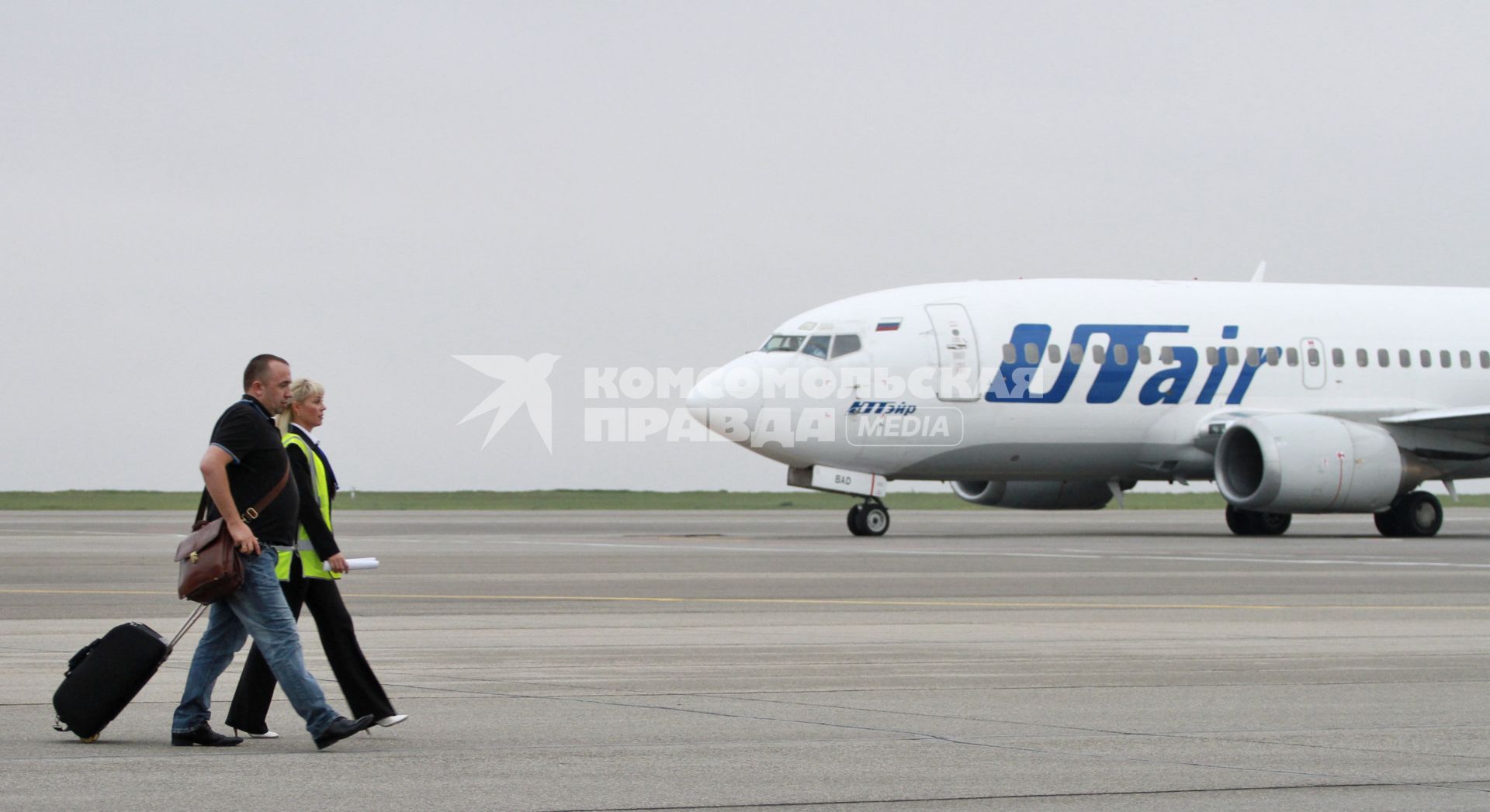 Пассажирский самолет Boeing 737-500 авиакомпания `UTair`. Пассажиры с чемоданами идут по взлетной полосе.