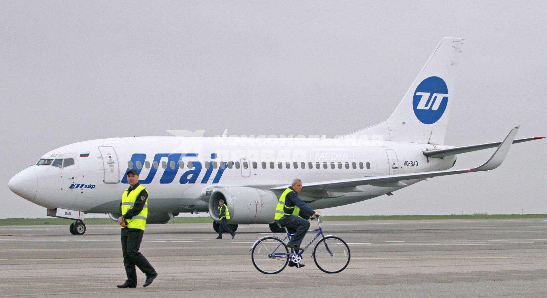 Пассажирский самолет Boeing 737-500 авиакомпания `UTair`. Служащий аэропорта едет по взлетной полосе на велосипеде.