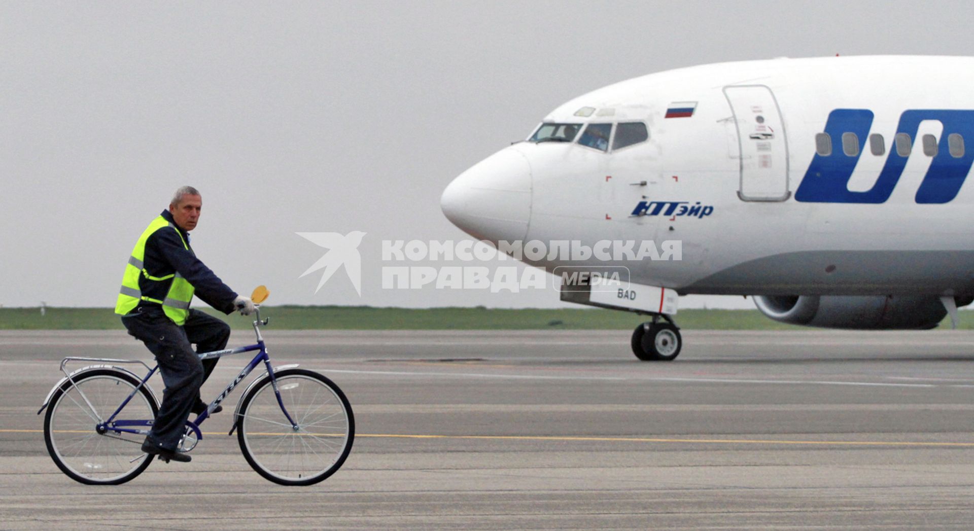 Пассажирский самолет Boeing 737-500 авиакомпания `UTair`. Служащий аэропорта едет по взлетной полосе на велосипеде.