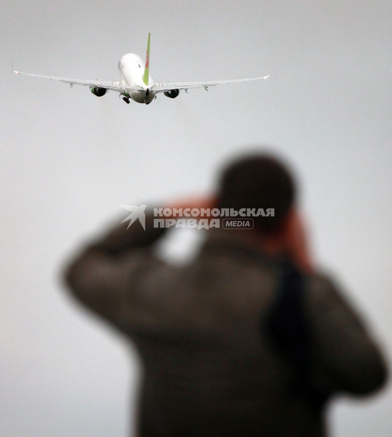 Мужчина фотографирует пассажирский самолет `Боинг 737-800` авиакомпании `S7`.