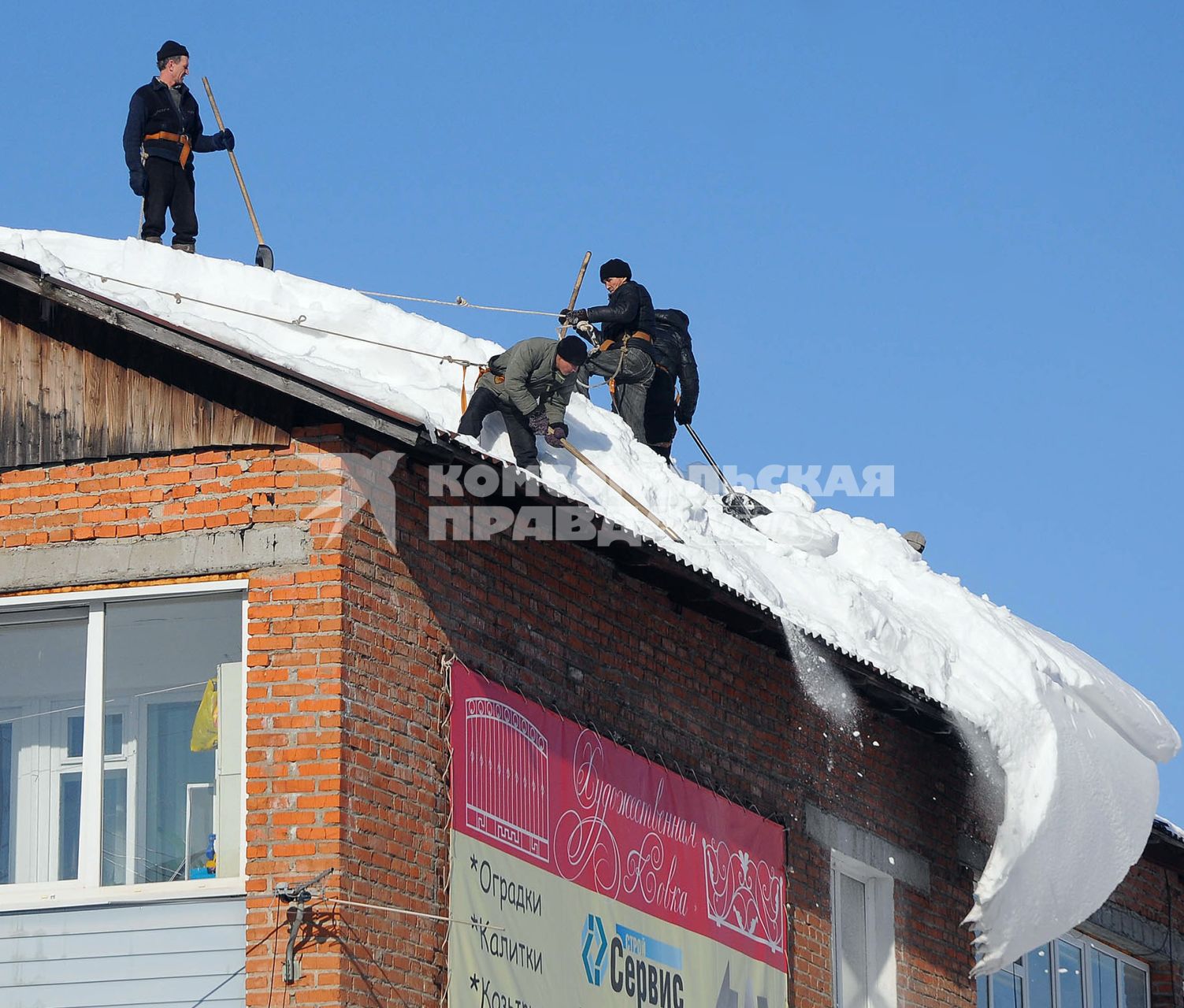 Рабочие отчищают крышу дома от снега.