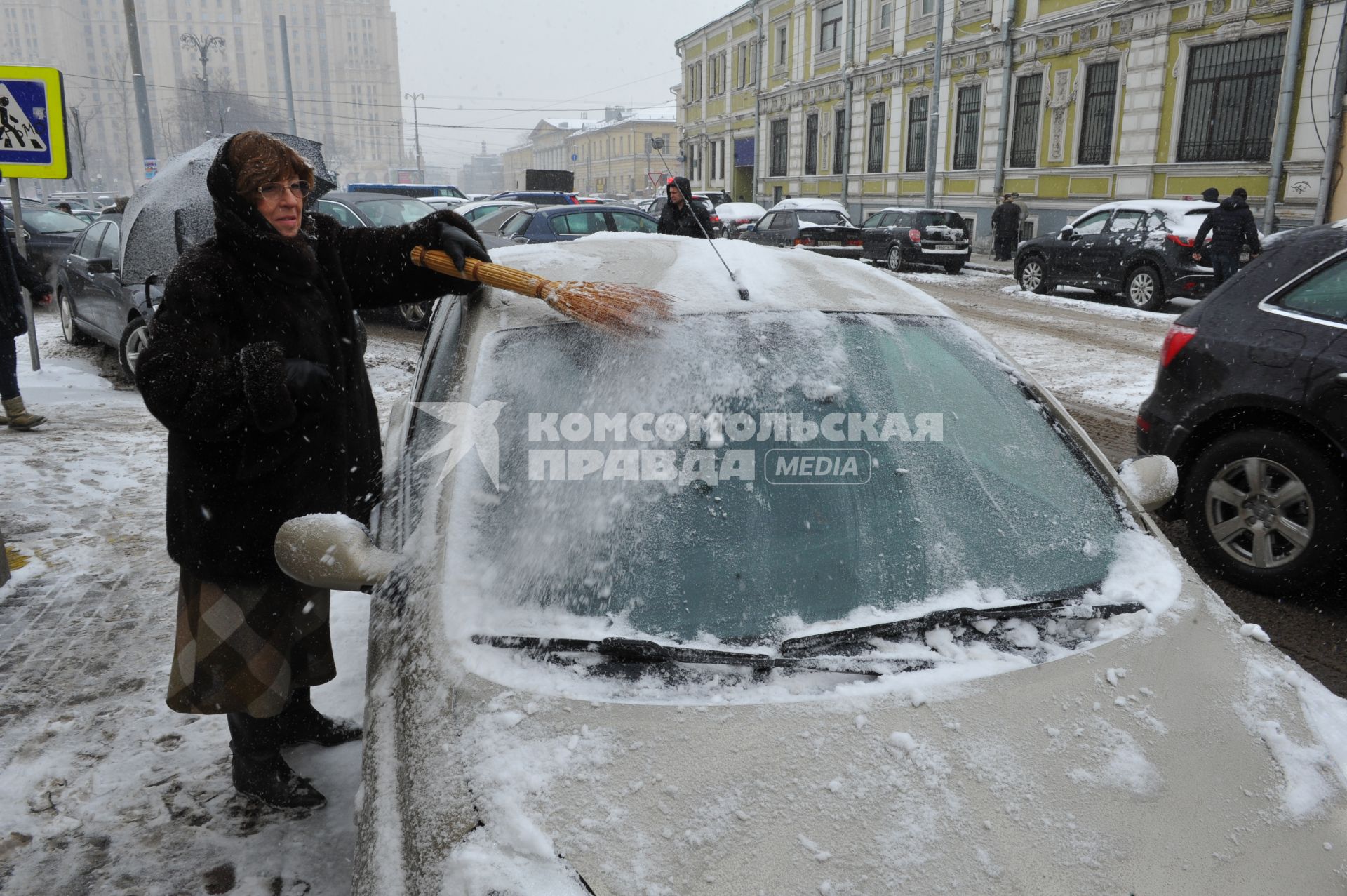 Женщина счищает снег с автомобиля.