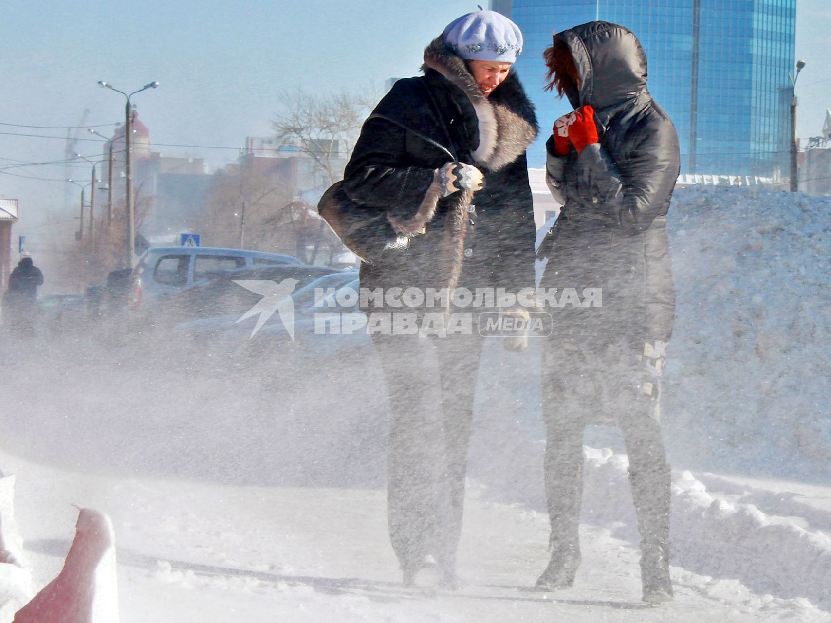 Женщины зимой на улице пытаются укрыться от метели.