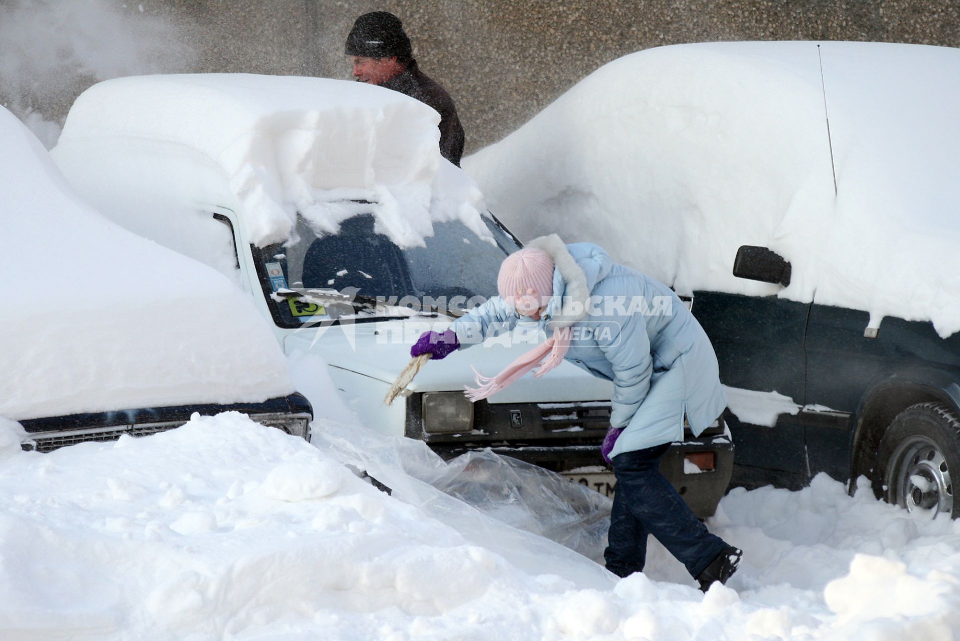 Последствия снегопада. Девушка счищает снег с автомобиля.