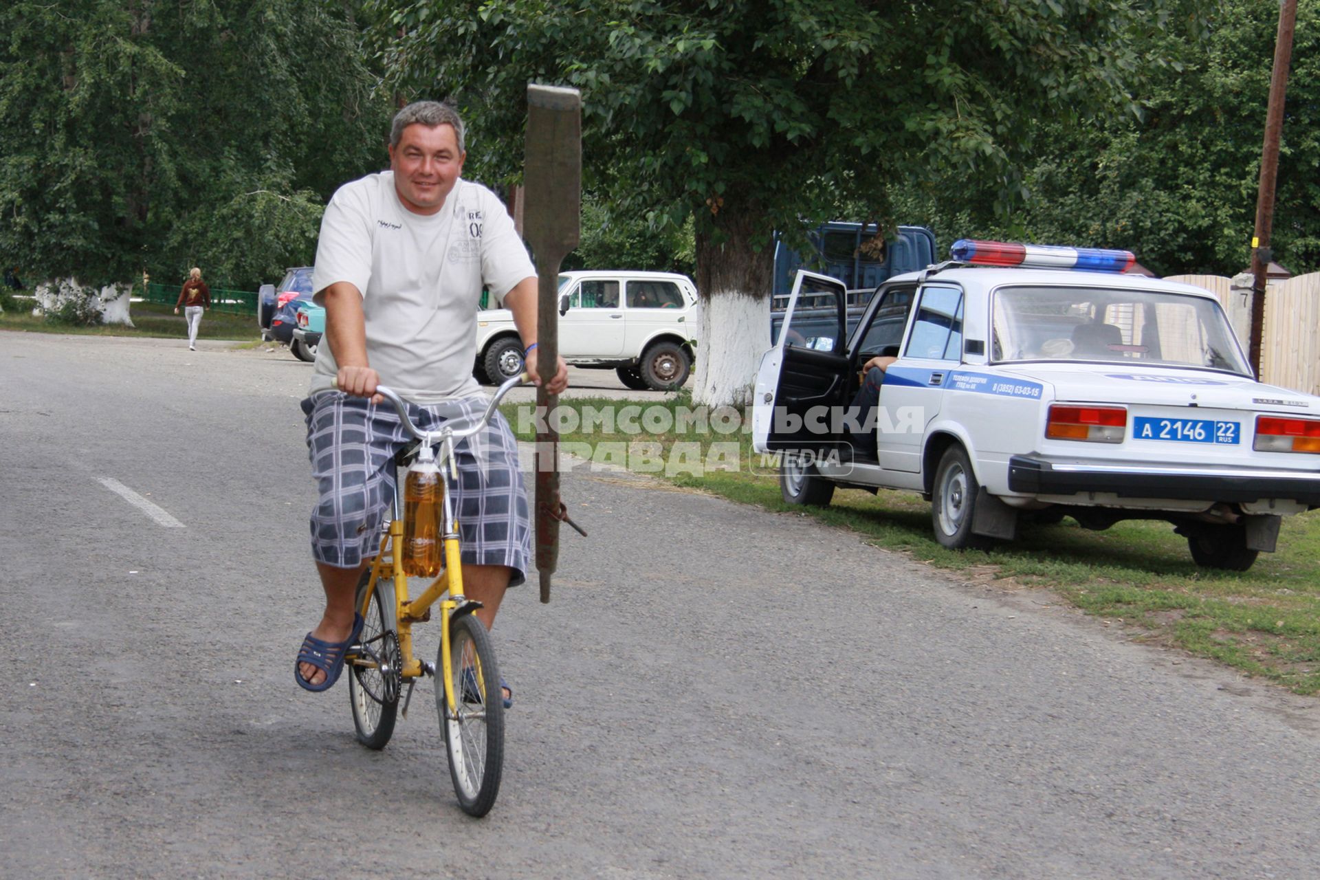 Мужчина с веслом едет на велосипеде мимо автомобиля полиции.