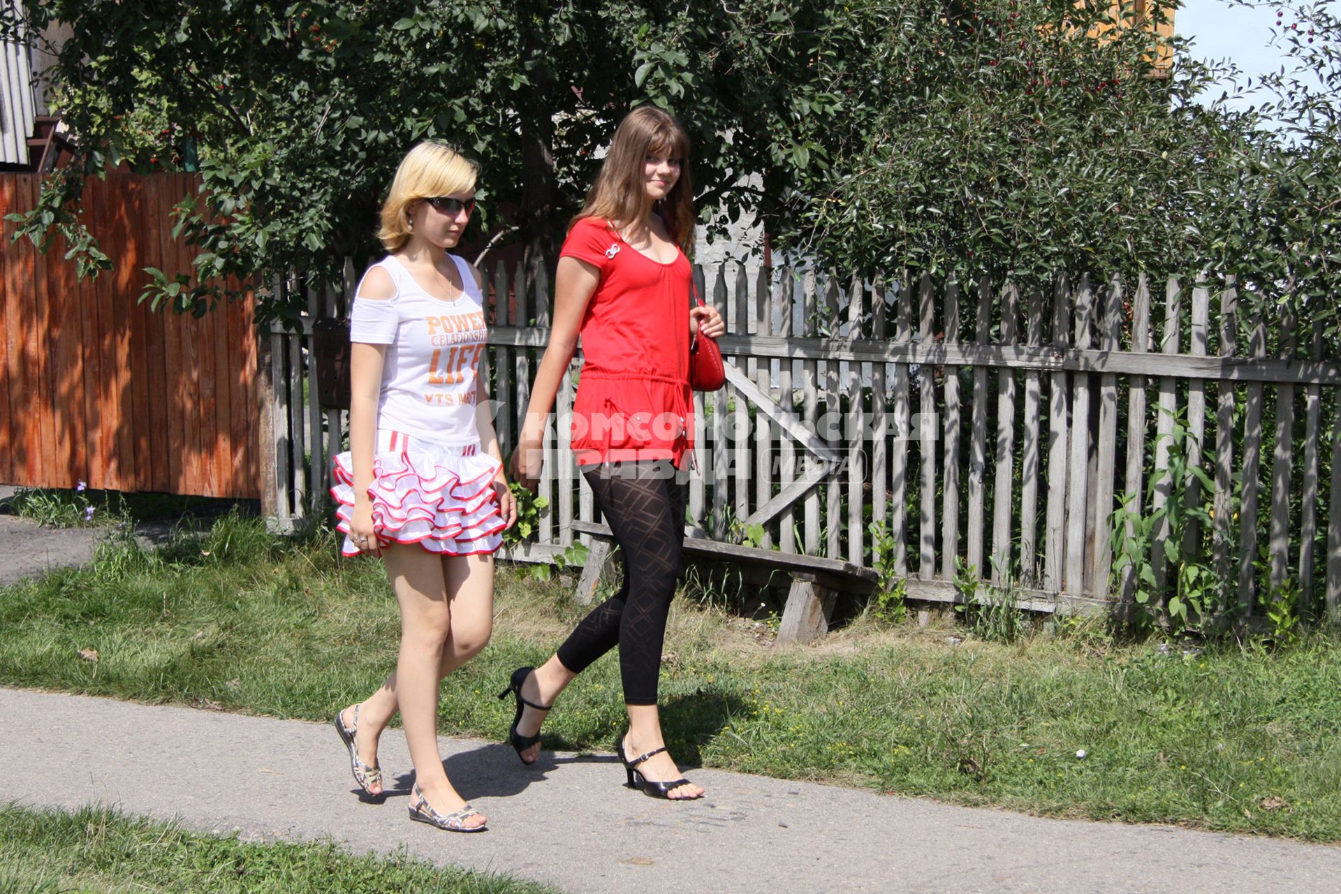 Две девушки идут по сельской улице.