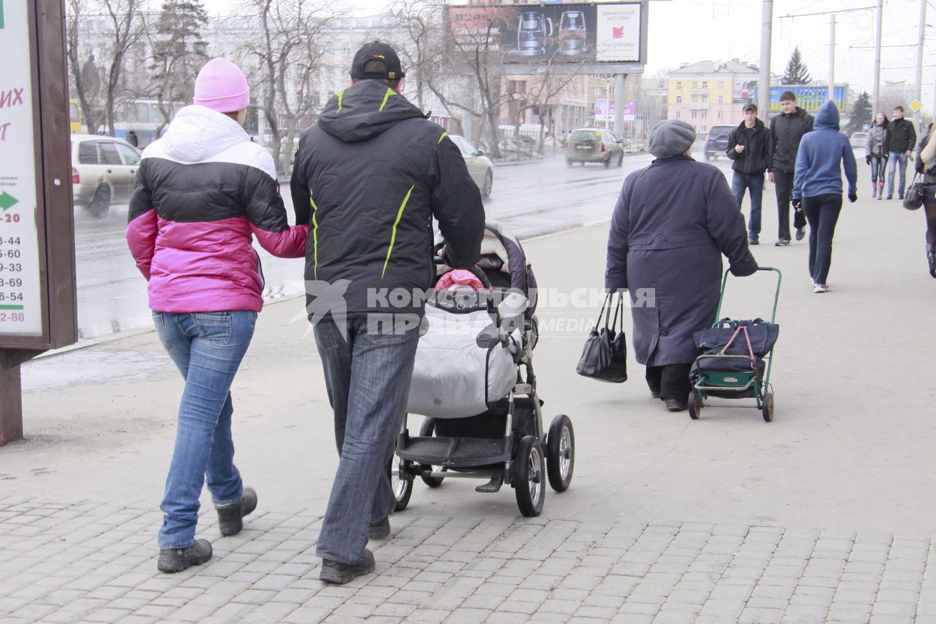 Мужчина и женщина гуляют с ребенком в детской коляске.