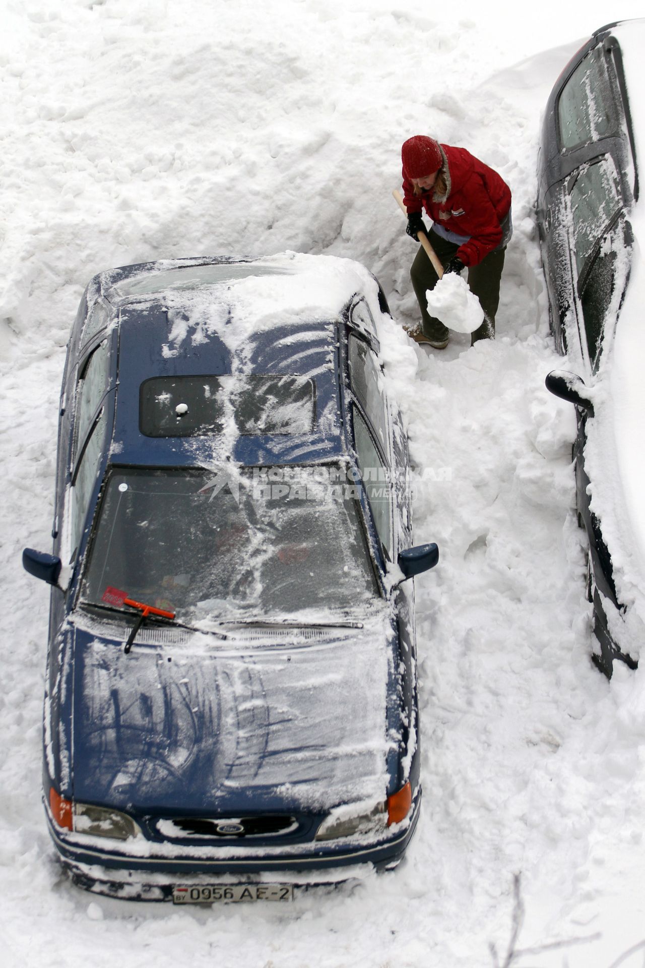 Женщина раскапывает занесенный во время снегопада автомобиль.