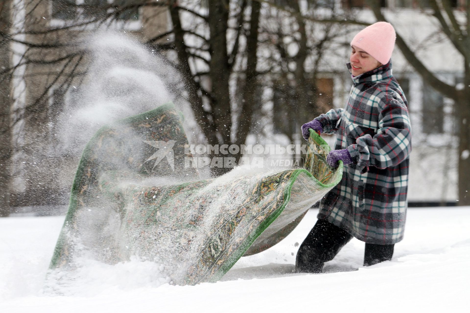 Юноша чистит ковер на снегу.