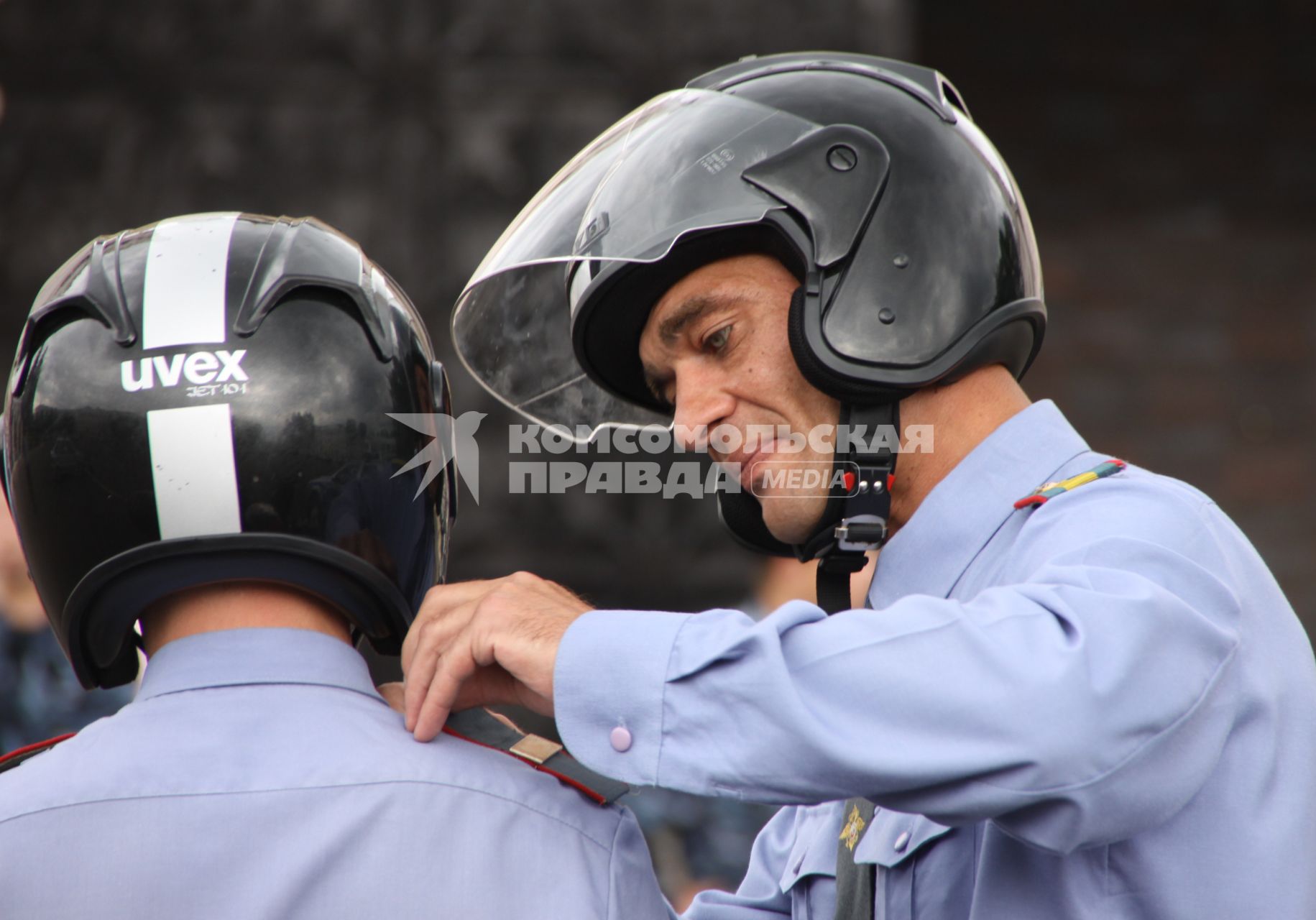 Полицейский помогает застегнуть мотоциклетный шлем другому полицейскому.