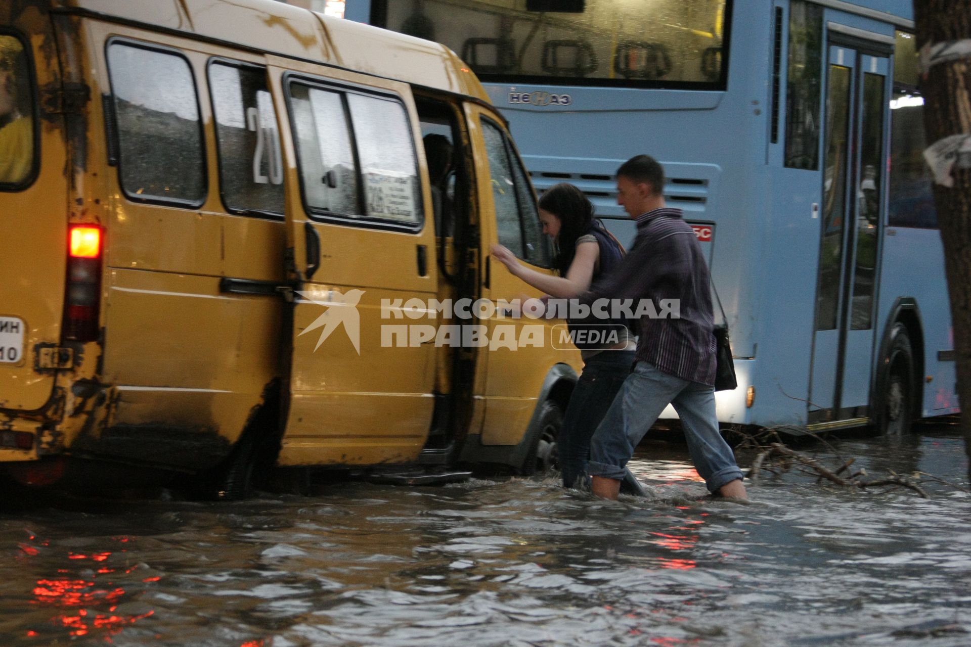 Молодые люди по колено в воде на затопленной улице после сильного ливня садятся в маршрутное такси.