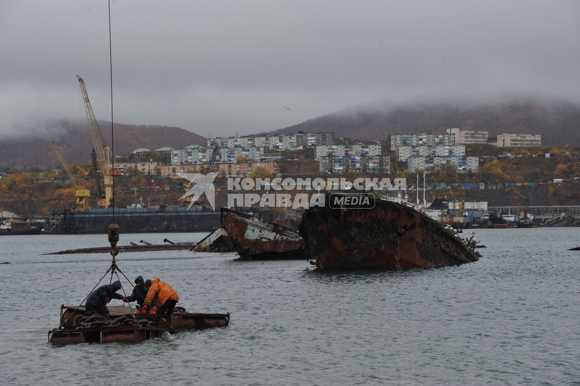 Петропавловск-Камчатский. Авачинская бухта. На снимке: рабочие поднимают с помощью грузовой техники ветхое судно со дна. На втором плане ветхие корабли.