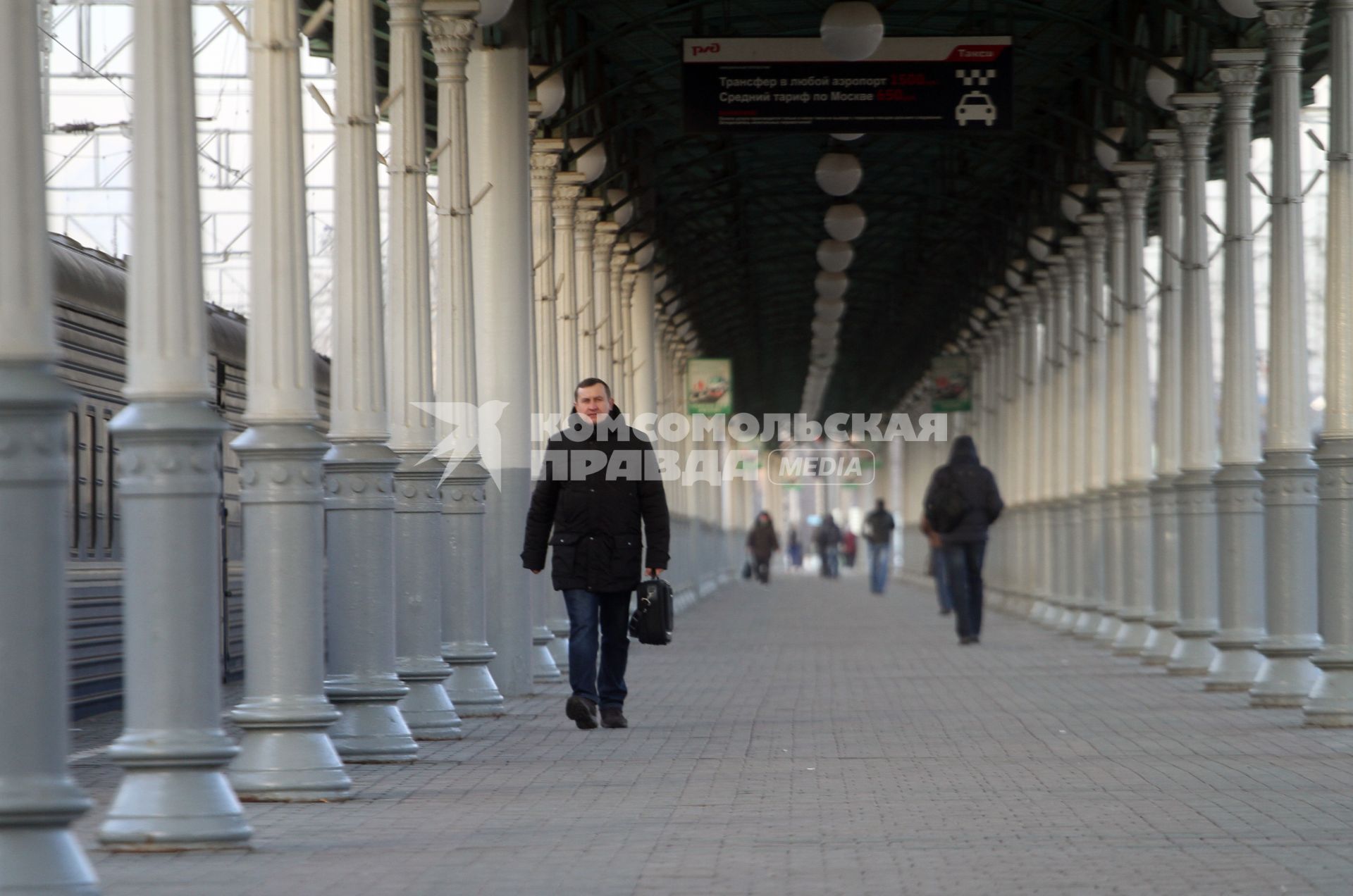 Мужчина с сумкой идет по платформе железнодорожного вокзала.