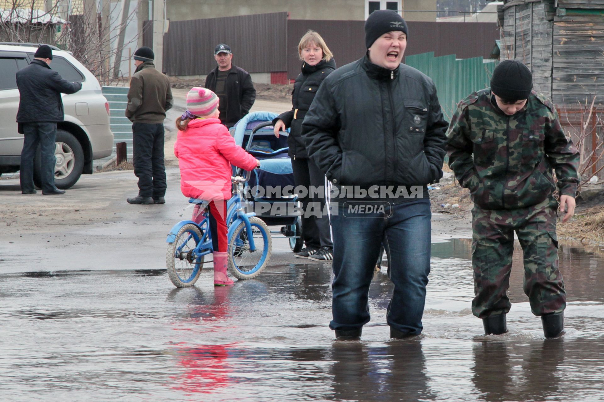 Молодежь идет по затопленной паводком улице по колено в воде.