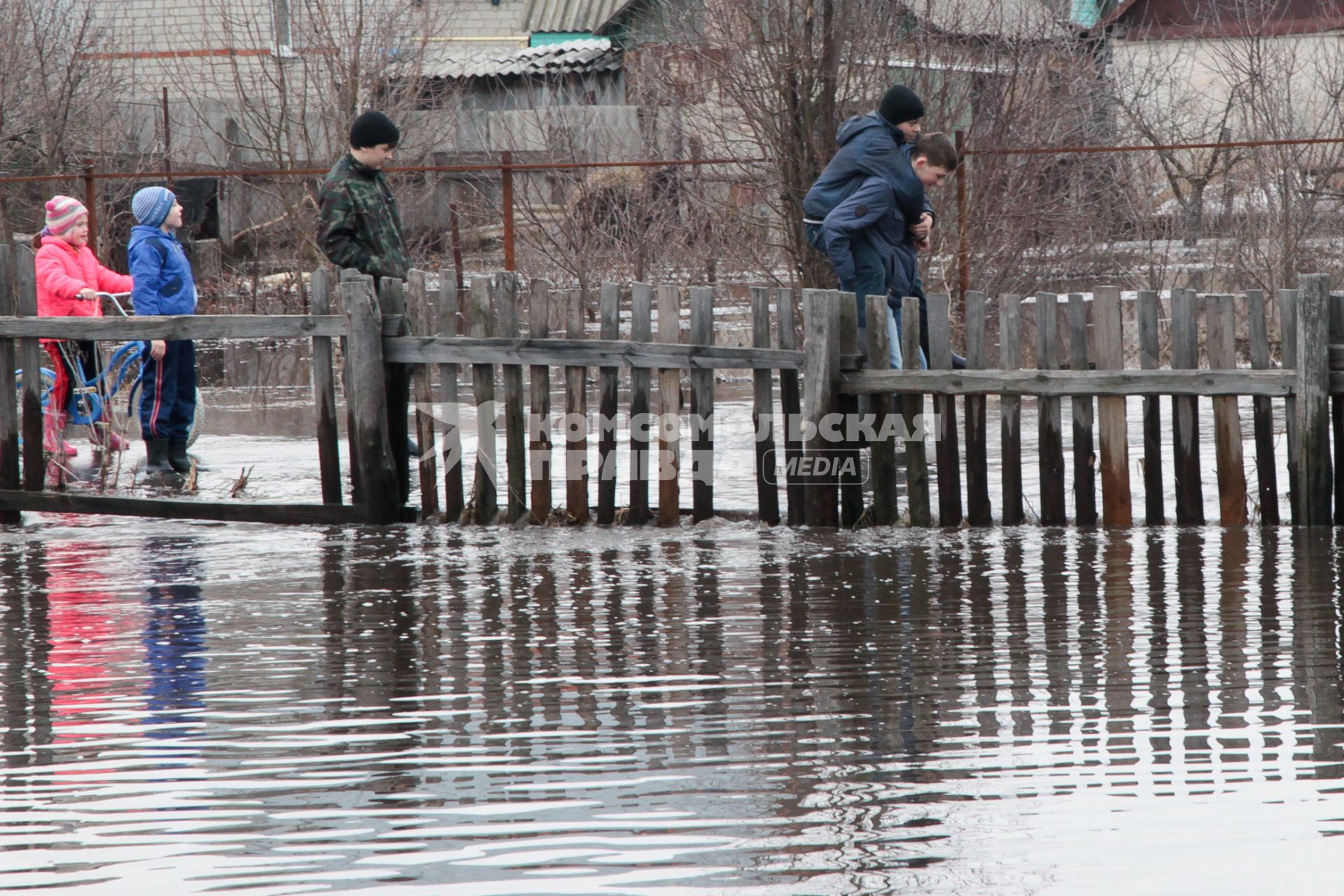 Молодежь идет по затопленной паводком улице по колено в воде.