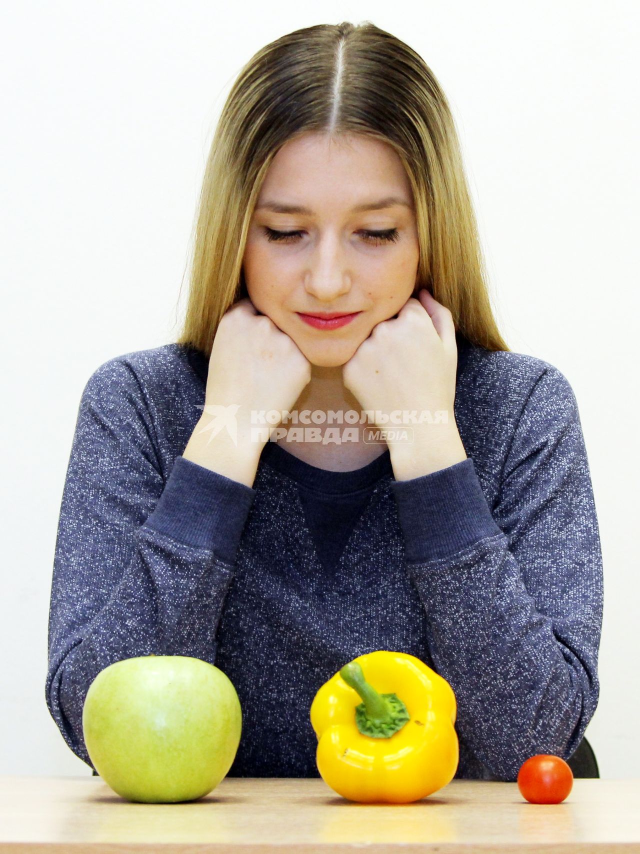 Девушка сидит и смотри на овощи.