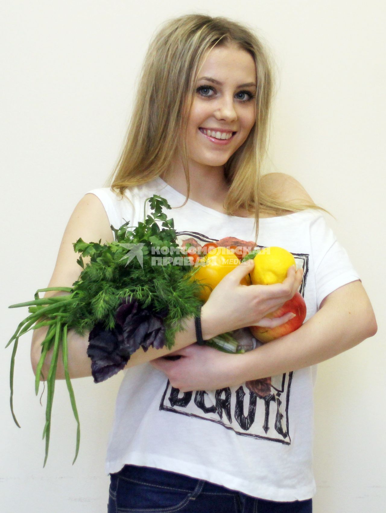 Девушка держит в руках овощи и фрукты.