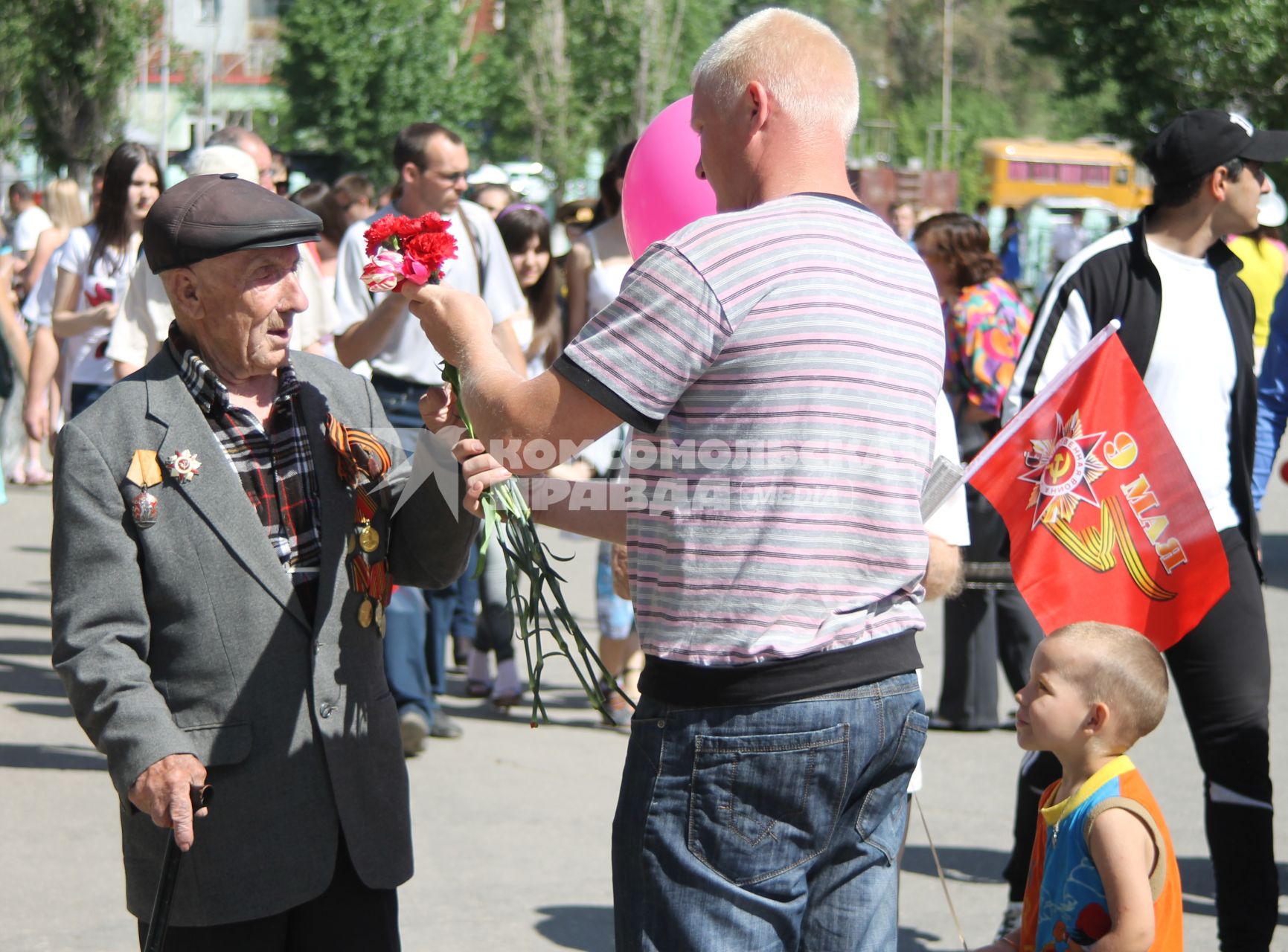 Мужчина с ребенком дарят ветерану гвоздики