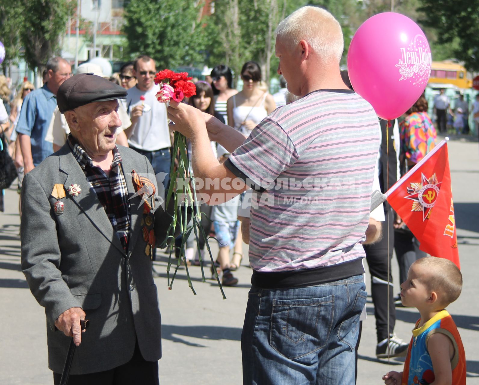 Мужчина с ребенком на 9 мая дарит ветерану гвоздики.