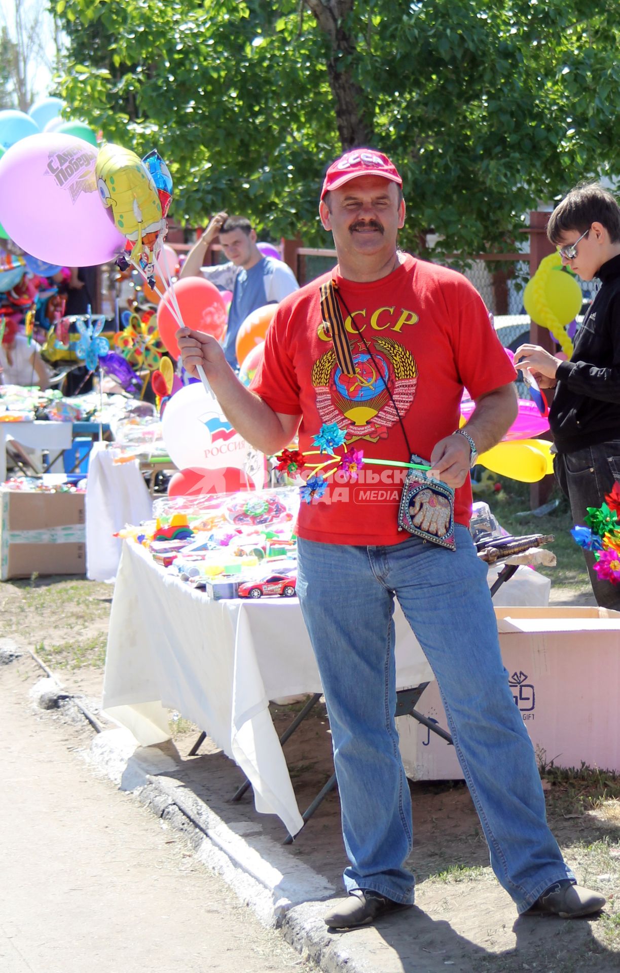 Мужчина в футболке с надписью СССР и в кепке держит в руках воздушные шары