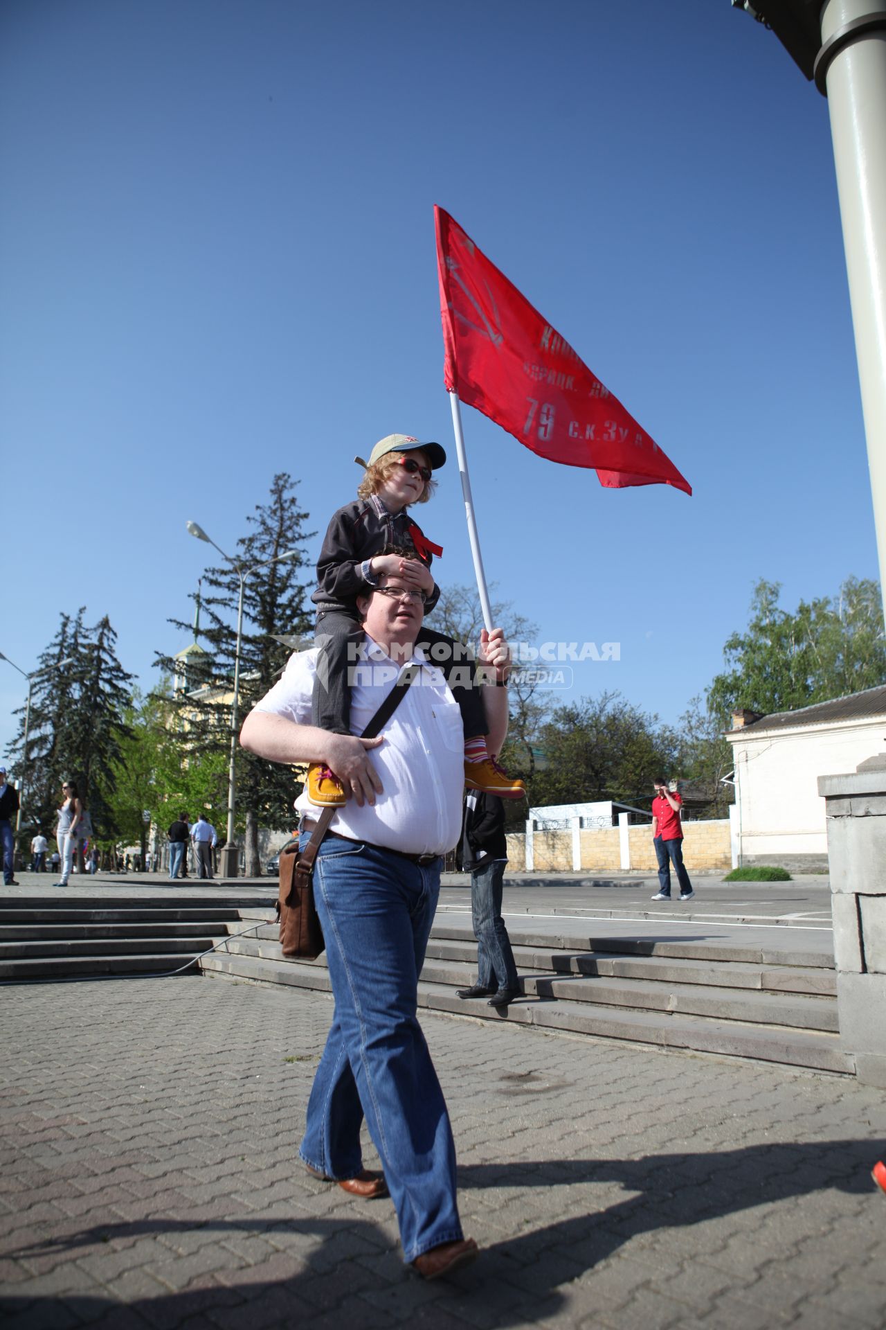 Мужчина несет мальчика на шее, у которого в руках красный флаг