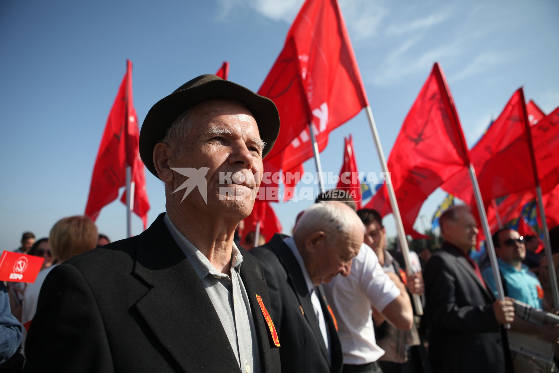 Пожилой мужчина на демонстрации, на фоне красных флагов