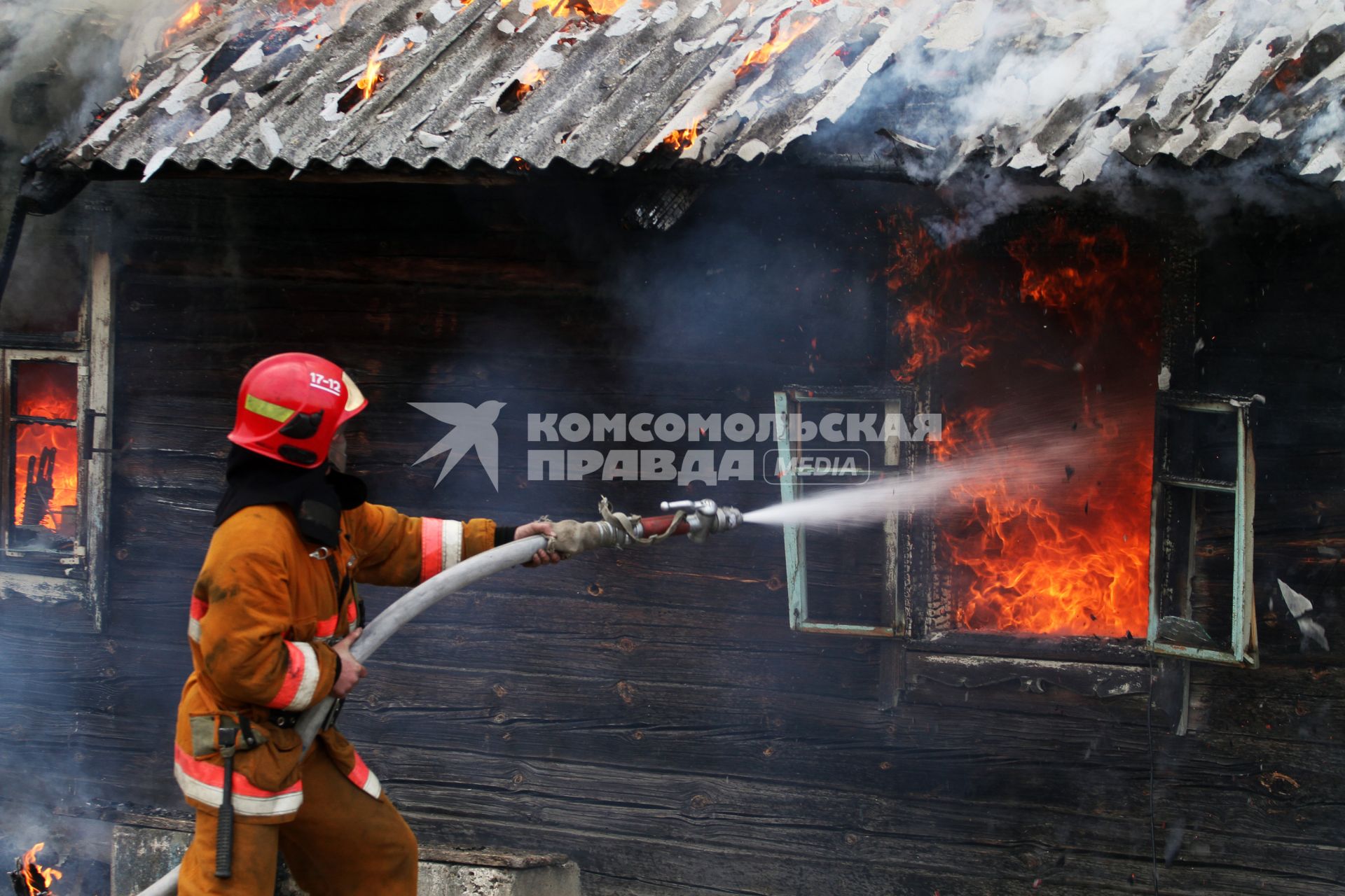 Пожарный тушит горящий дом