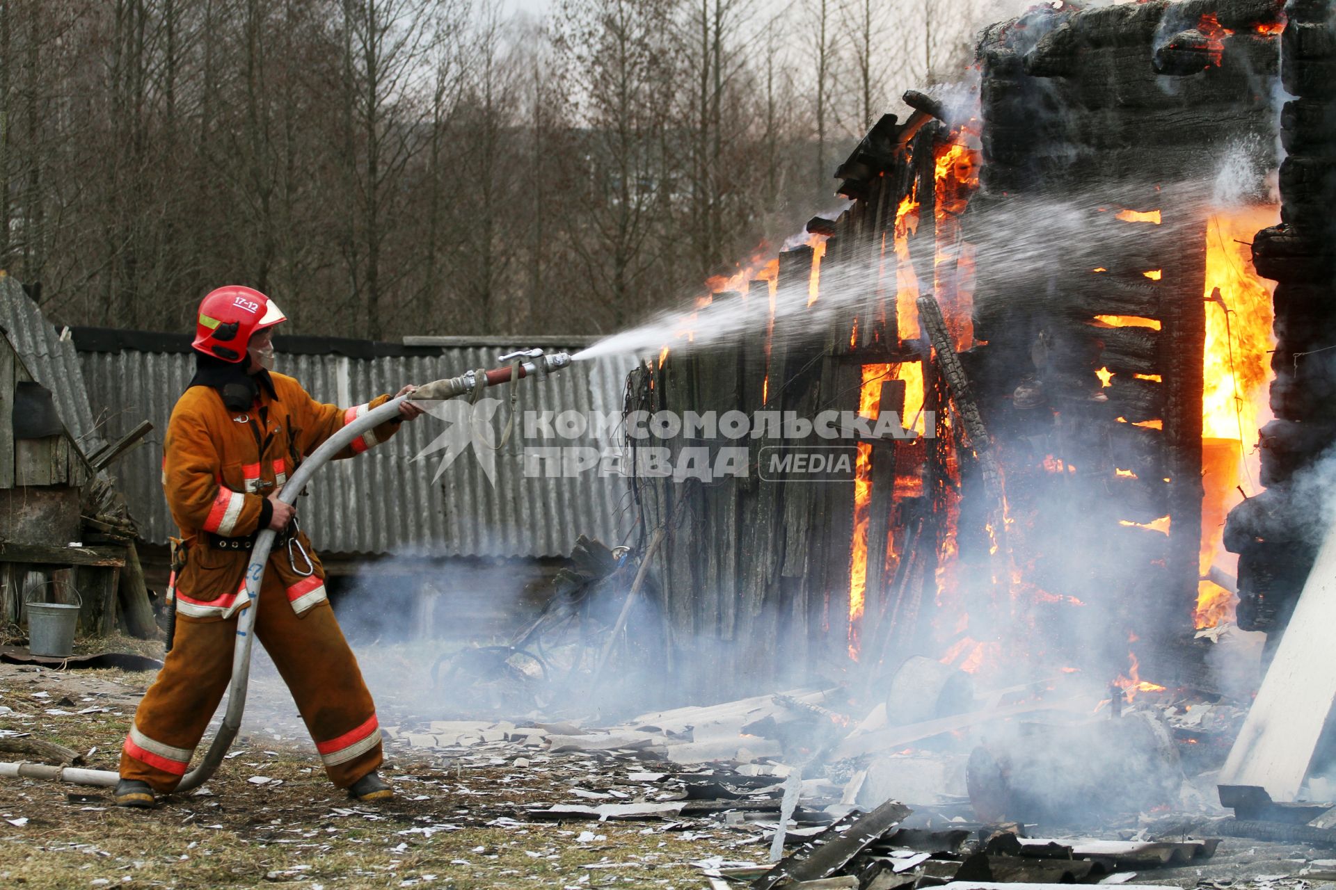 Пожарный тушит горящий дом